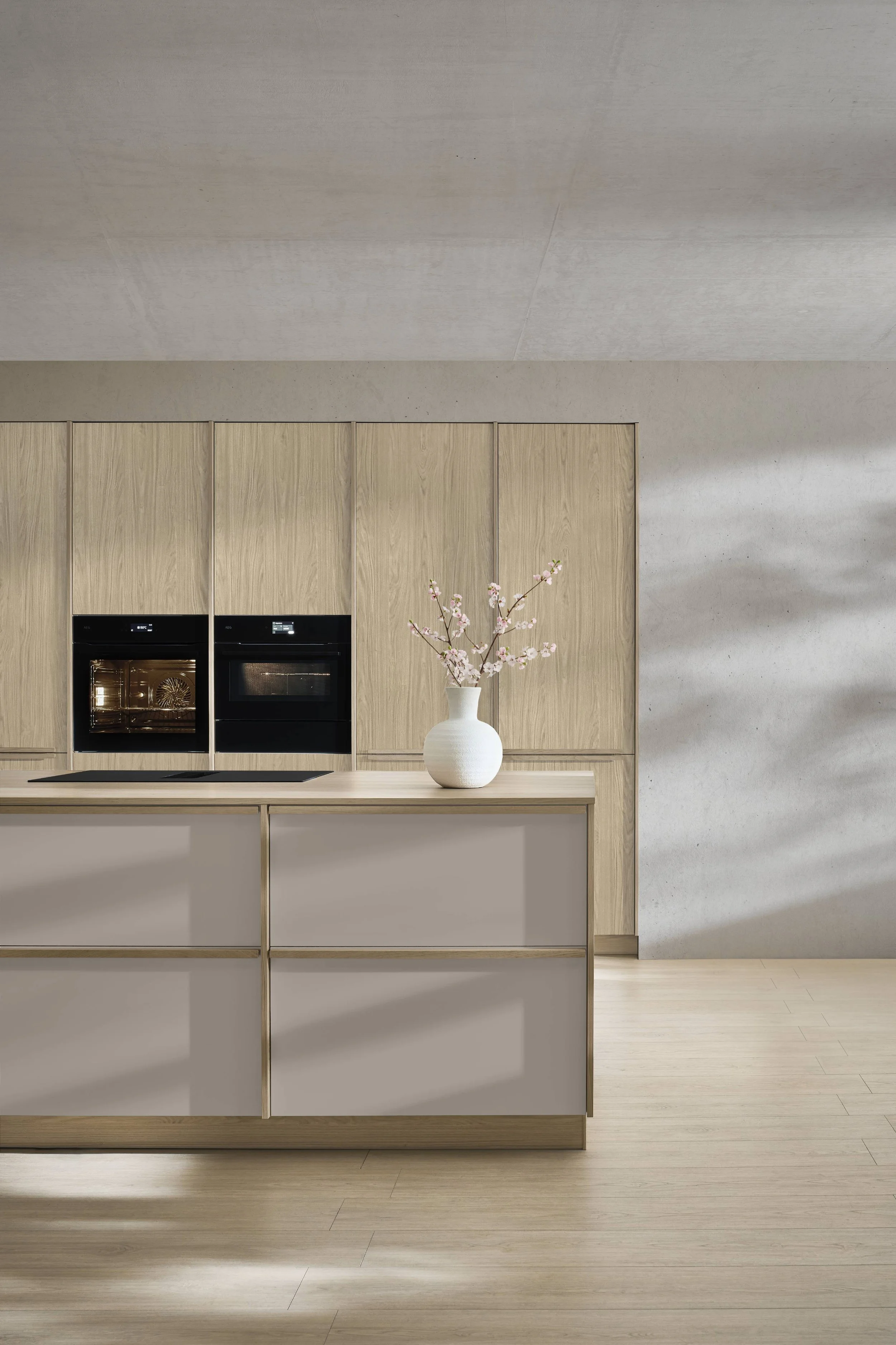 Moderne Küche mit Holzschrank, Kücheninsel, weißer Vase mit pinken Blüten, Backofen und Herd.