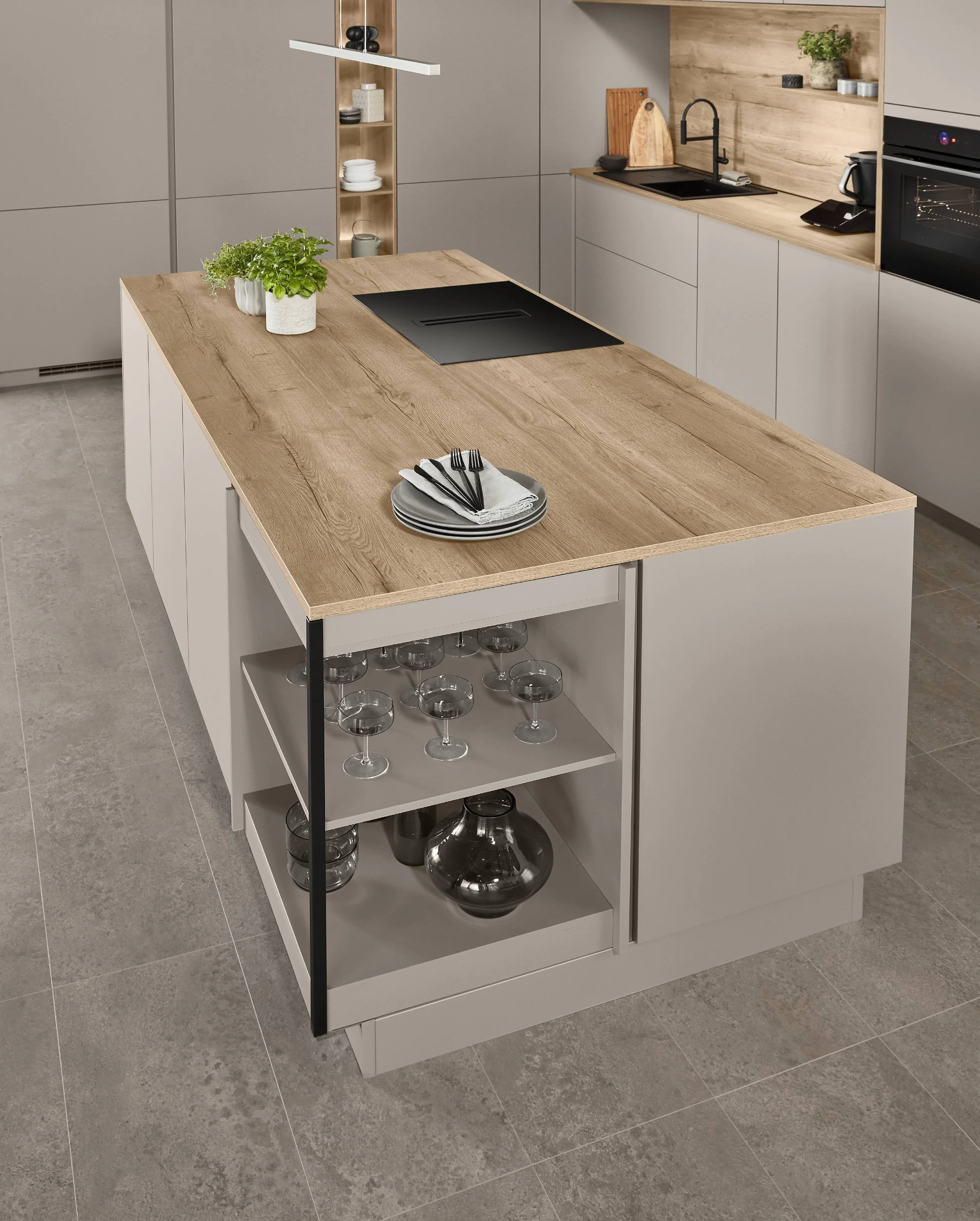 Moderne Küche mit Holztisch und weißem Unterschrank, auf dem Tisch stehen Teller, Besteck und eine Pflanze, im Hintergrund Küchenutensilien und Geräte.