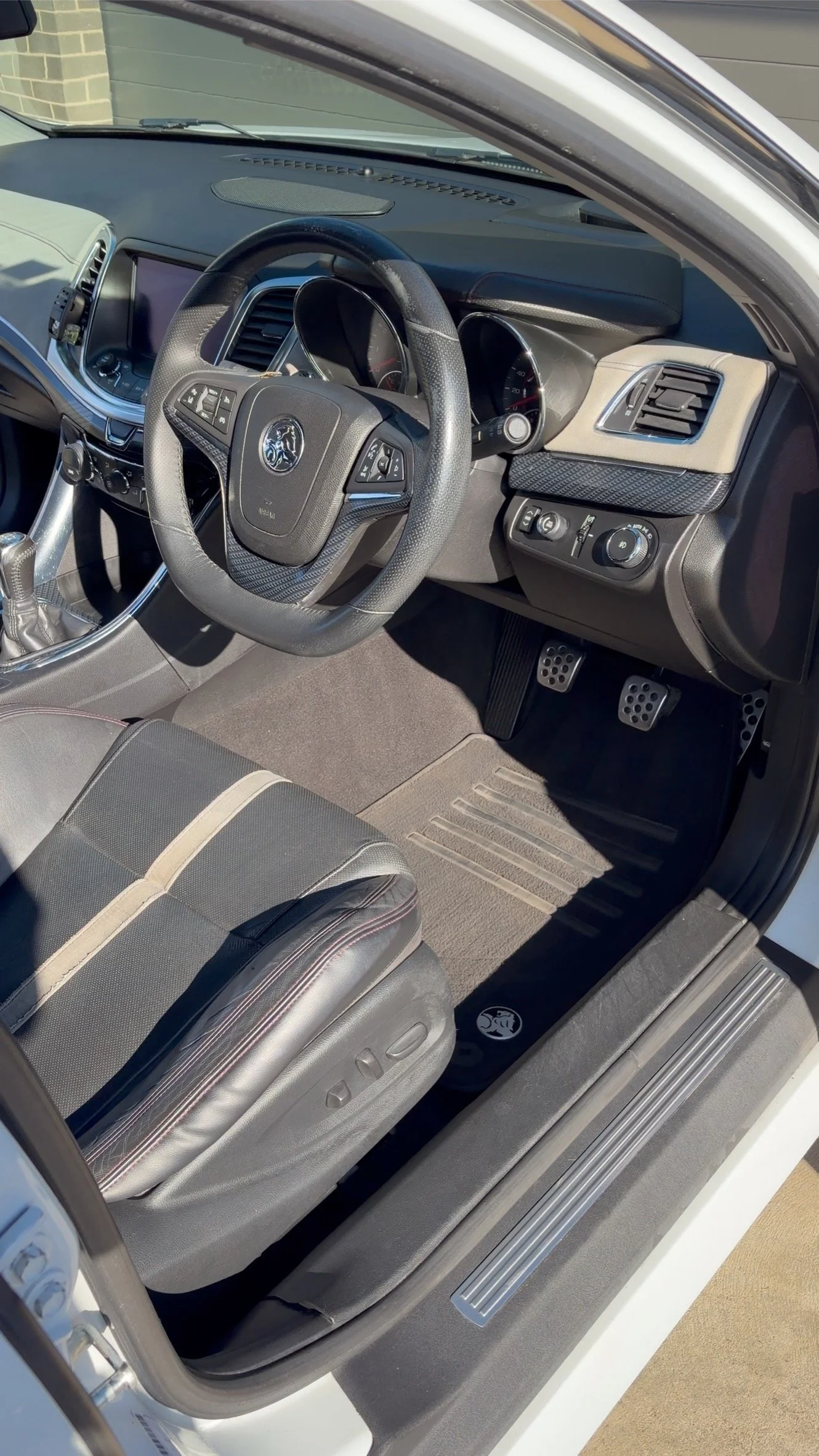 Inside the front of a car showing the steering wheel, dashboard, gear shift, driver's seat, and floor mats.