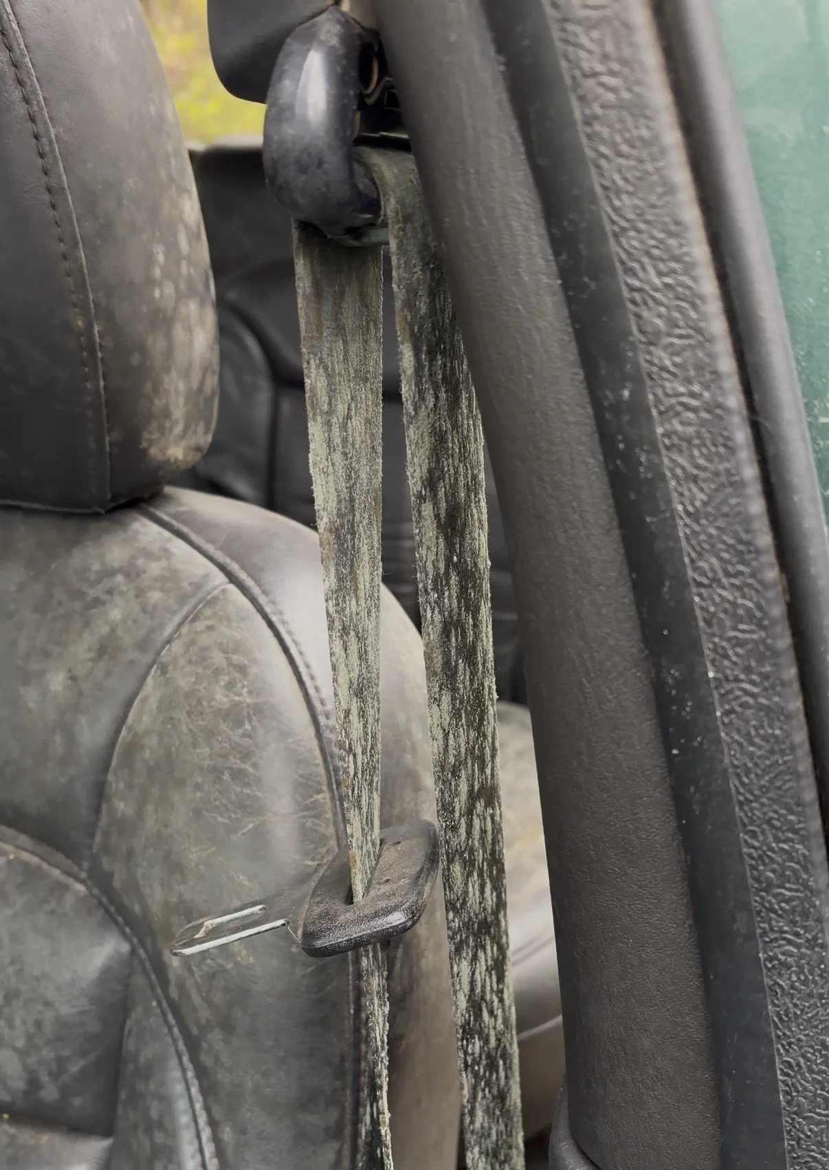 Close-up of a dirty metal lock and a weathered metal latch on a car seat, with black plastic trim and textured black interior door panel visible.