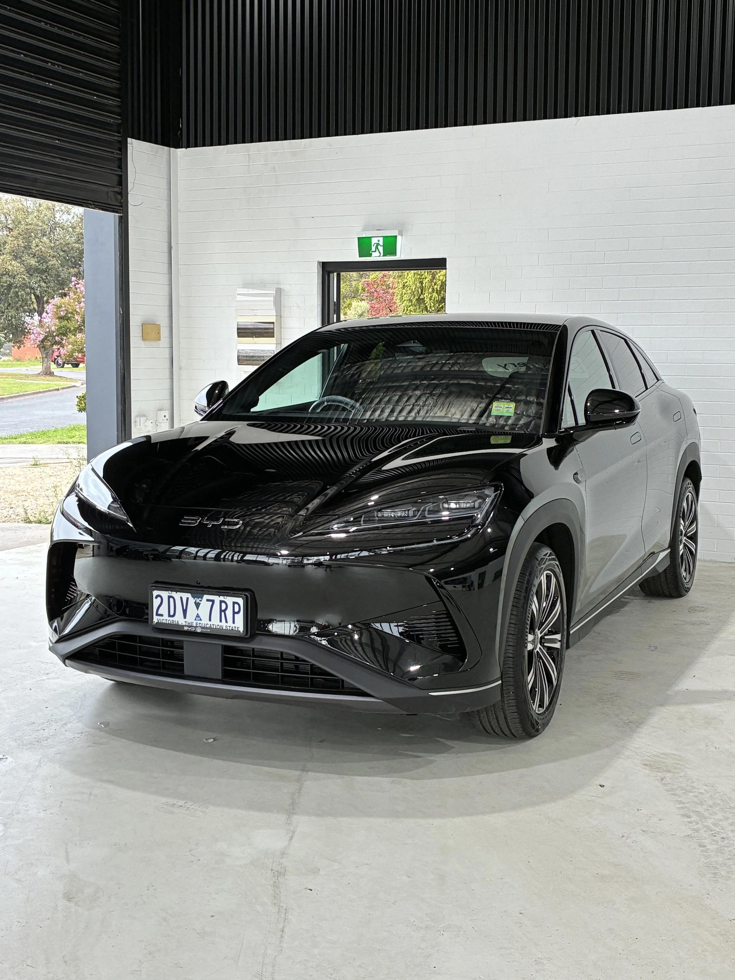 Black Hyundai Ioniq 5 parked inside a modern building with white brick wall and large window, emergency exit sign above the door.