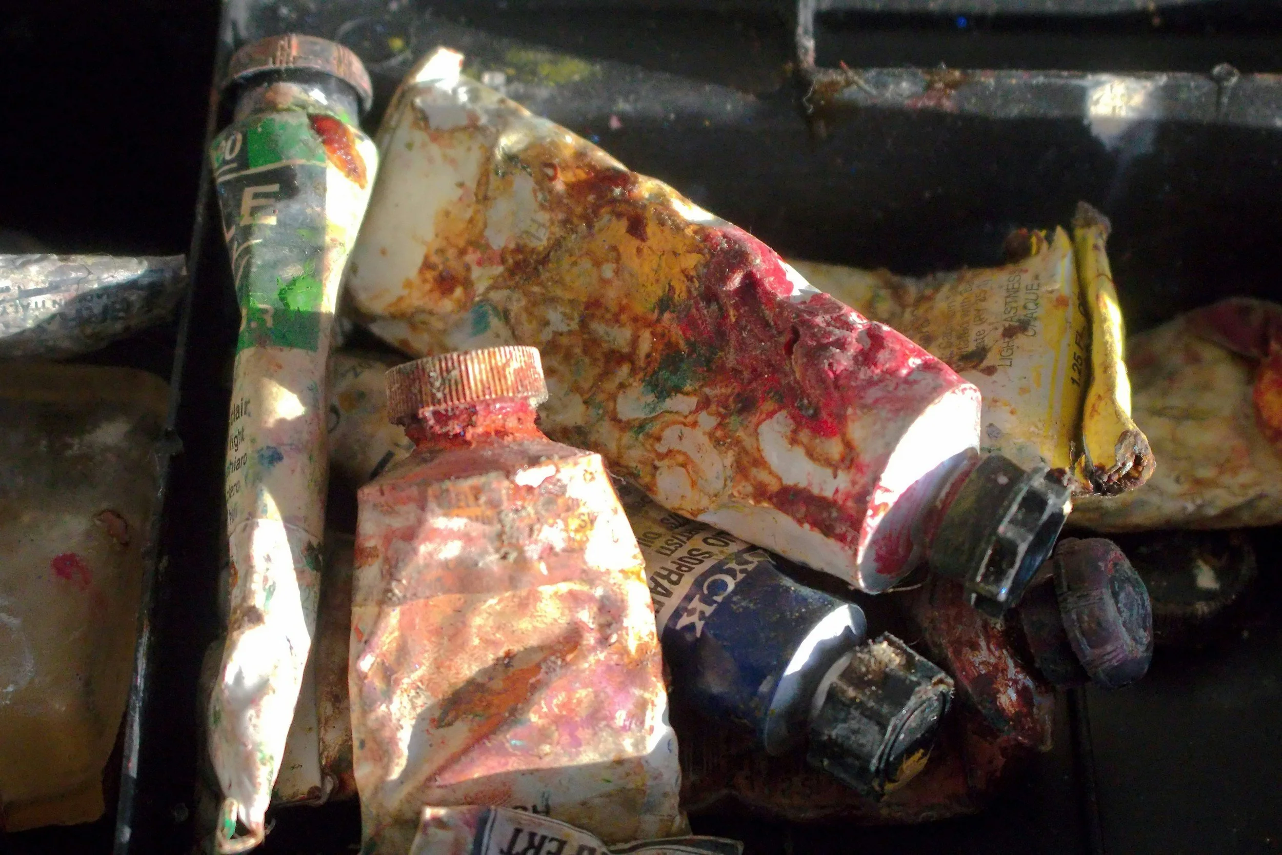 Close-up of a collection of old, dirty, and paint-splattered paint tubes.