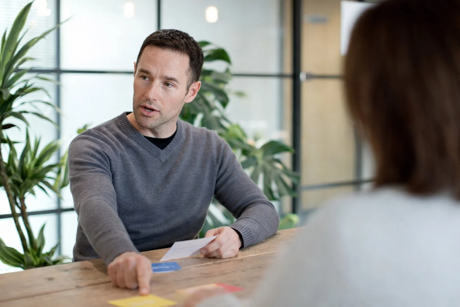 Man pointing at a sticky note, sitting at a desk in a modern office environment