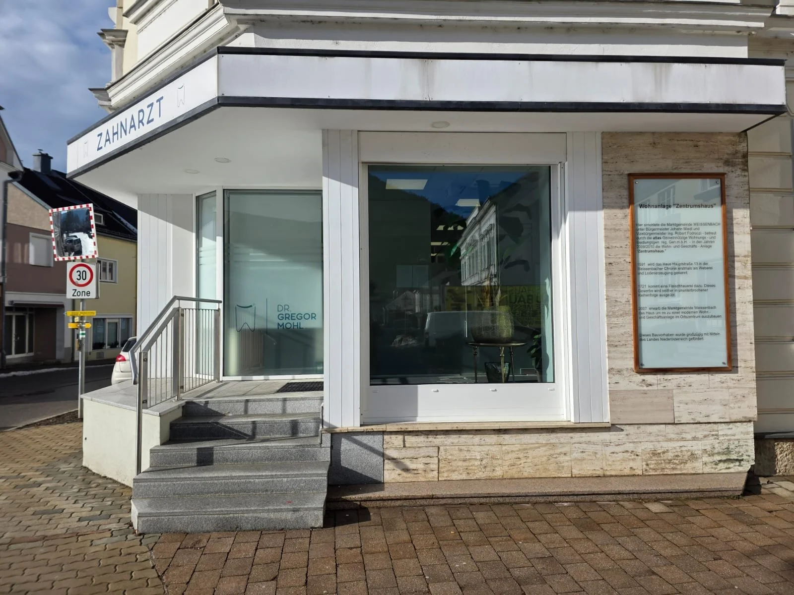 Frontansicht eines weißen Gebäudes einer Zahnarztpraxis, Stufen und einem Weg.