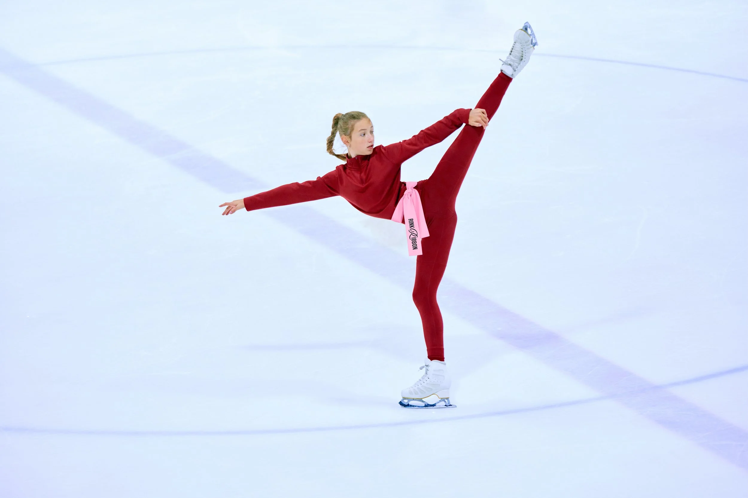 Figure skater wearing a neon Rink Ribbon™ during a program run-through at an indoor ice rink.