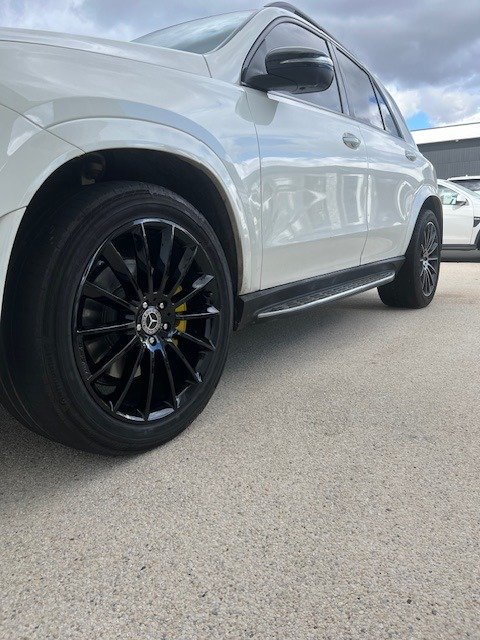 Side view of a white luxury SUV with black wheels parked on a light gray asphalt surface, under a cloudy sky.