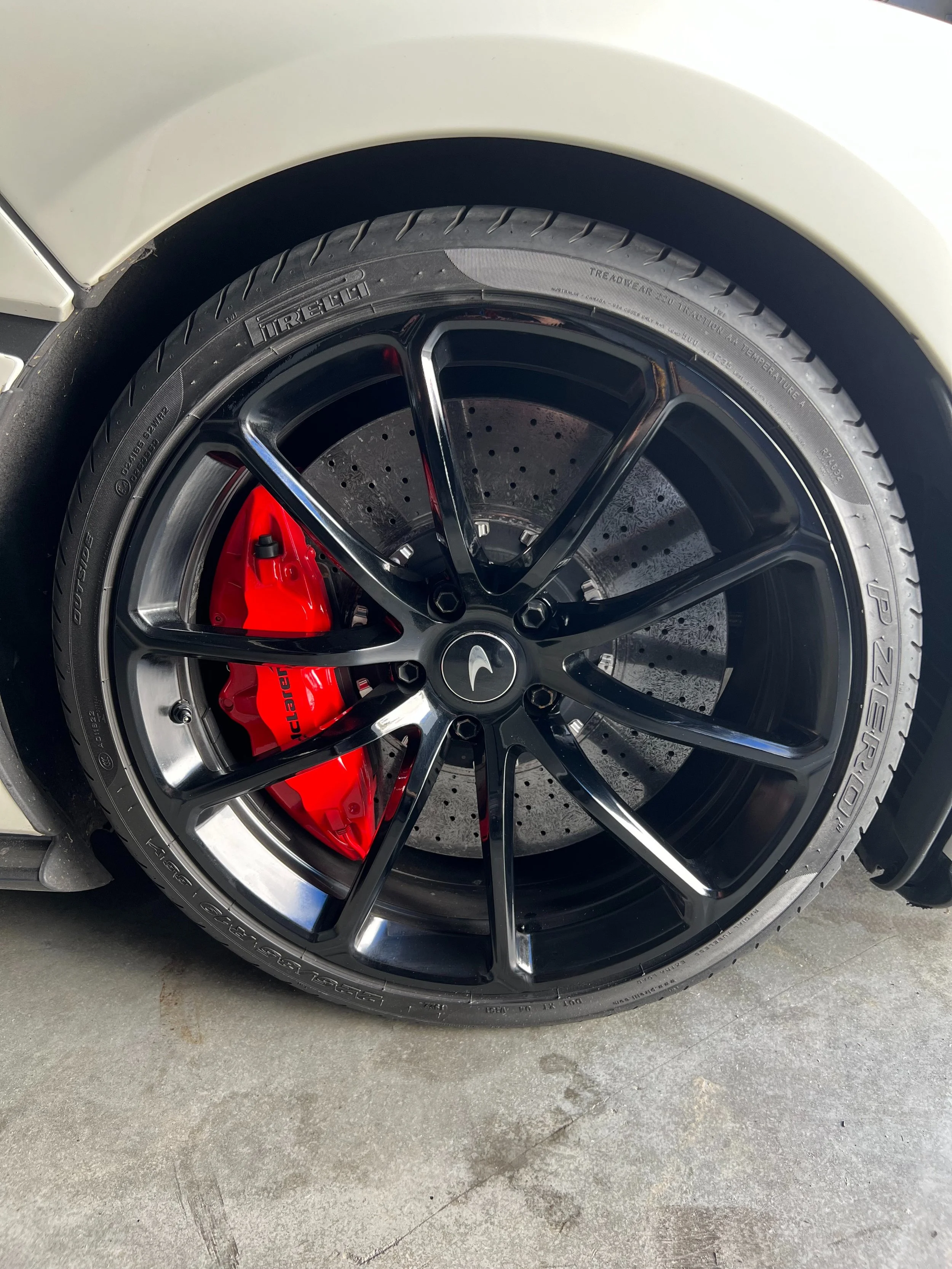 Close-up of a luxury car wheel with a black rim, red brake caliper, and perforated brake disc.