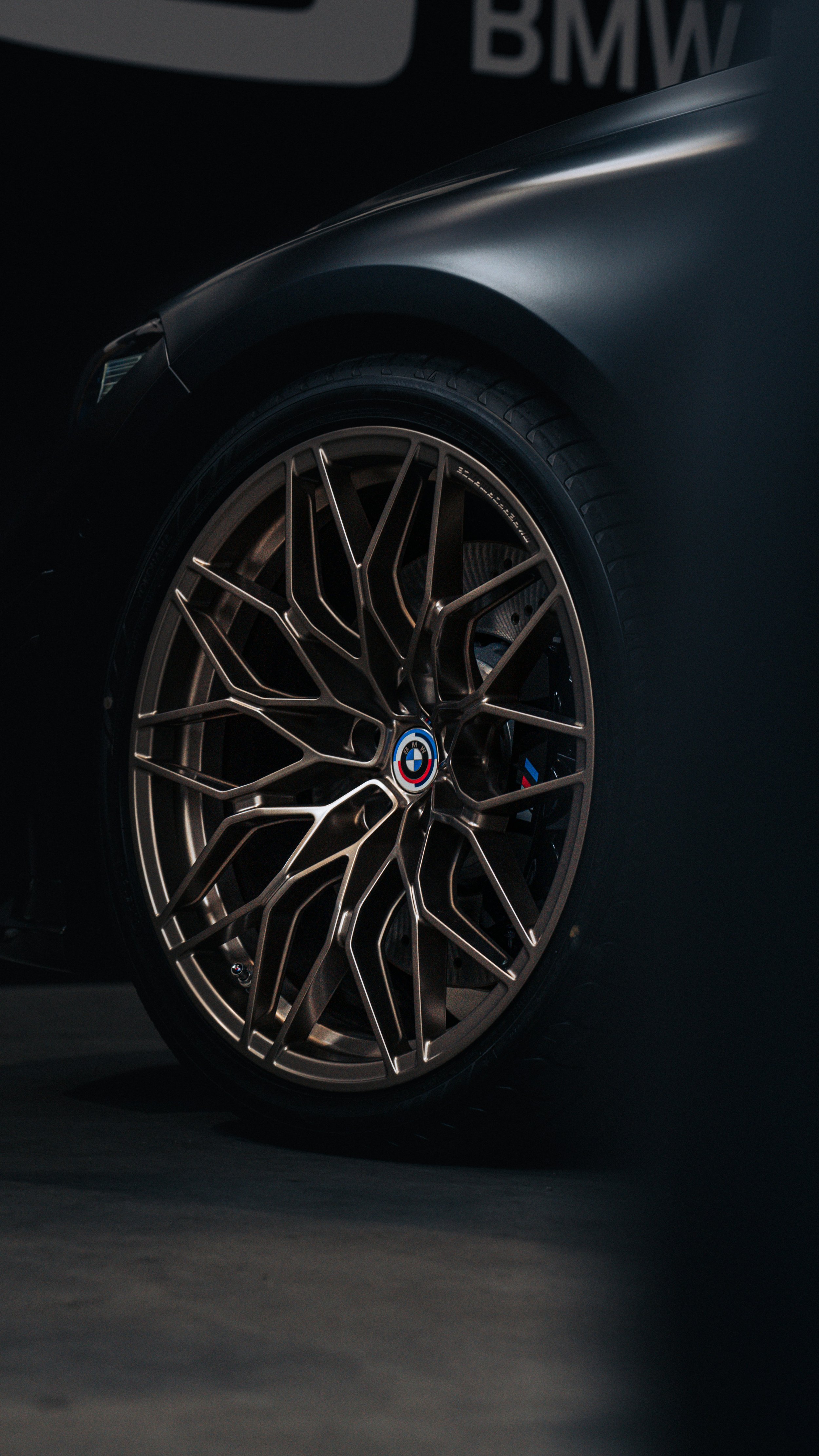 Close-up of a BMW car wheel with a sleek, multi-spoke alloy rim featuring the BMW logo at the center, set against a dark background.