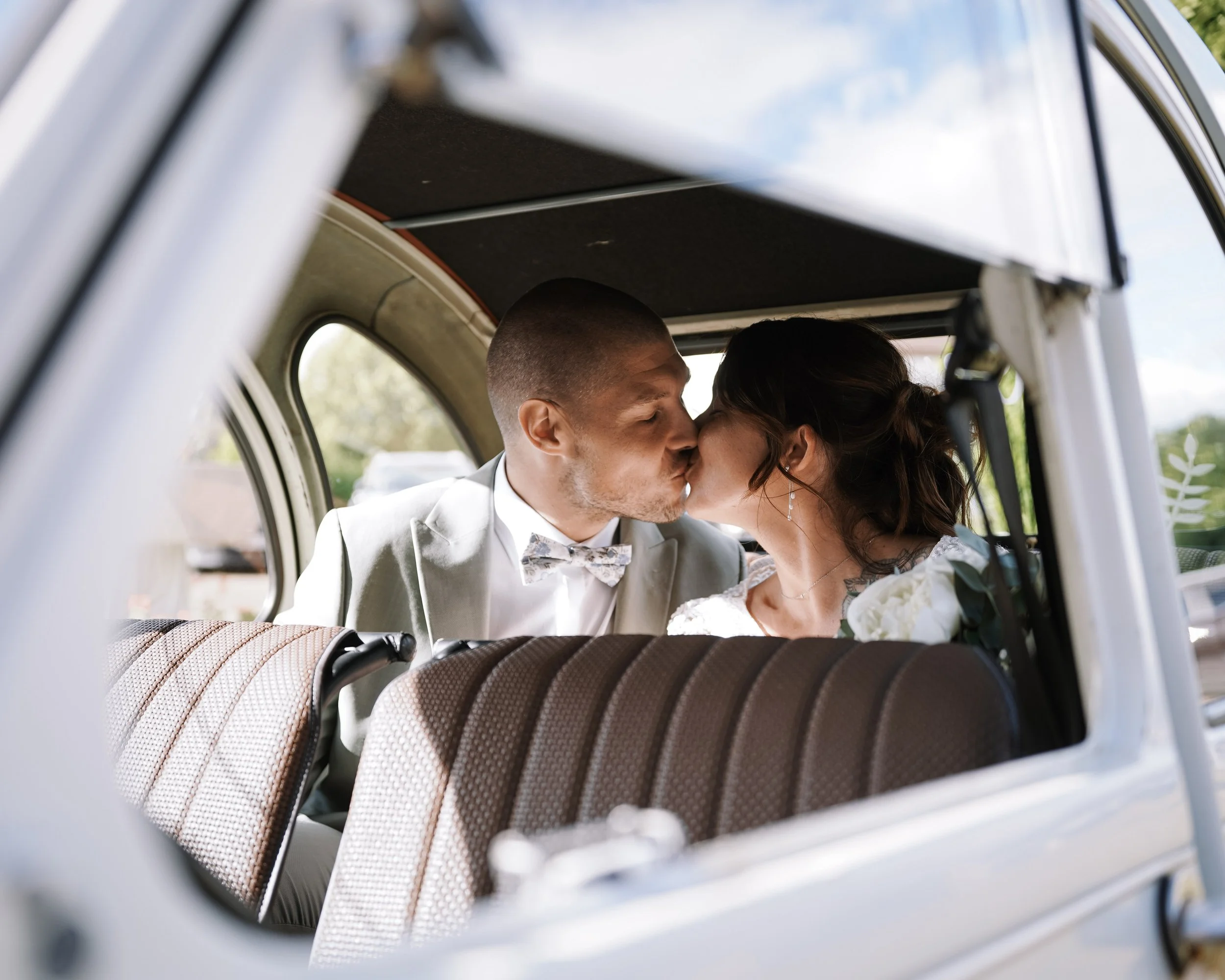 Un couple en mariage partage un baiser dans le véhicule, vu à travers la fenêtre.