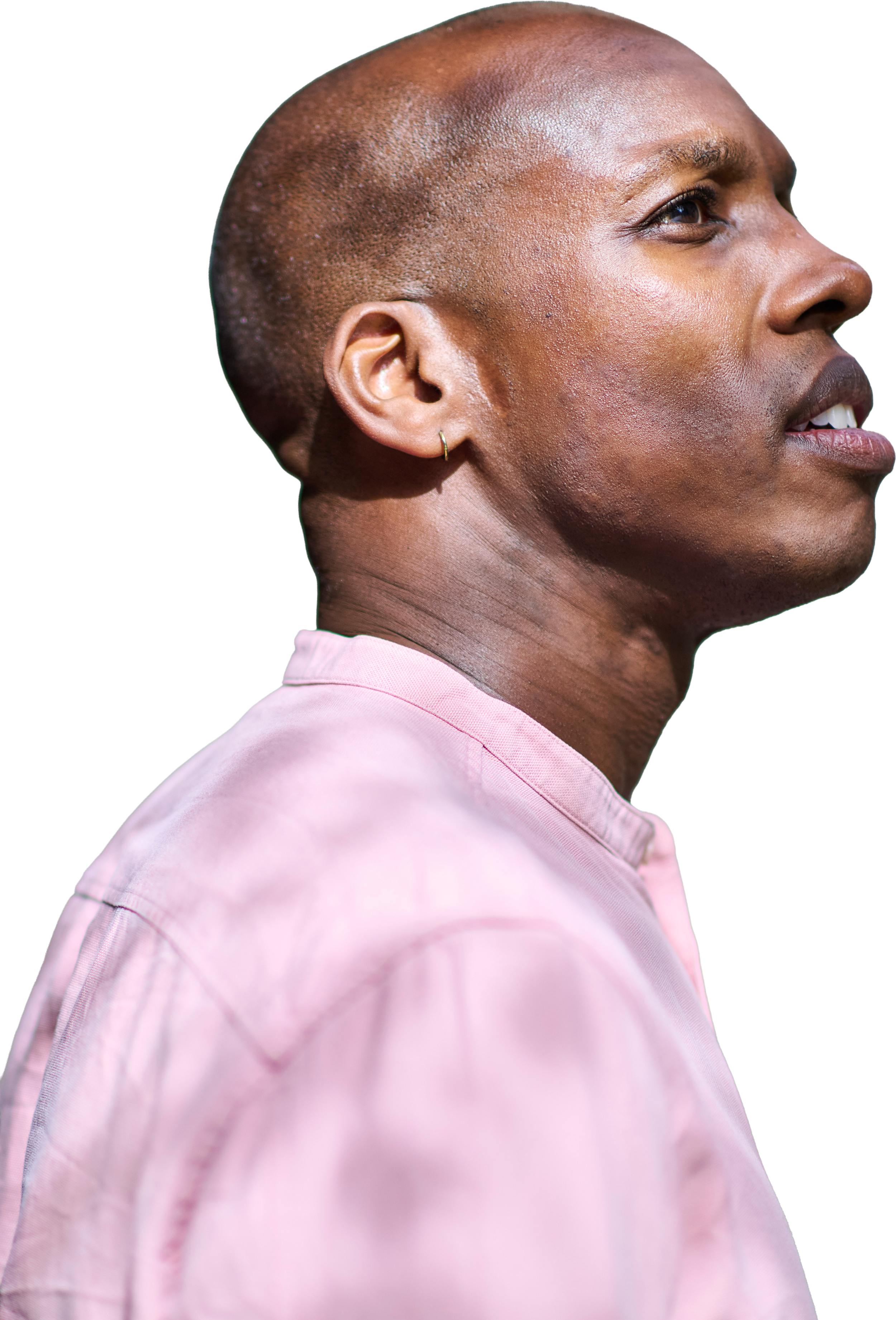 Close-up side profile of an African American man with a shaved head, wearing a light pink shirt and small hoop earring, against a black background.