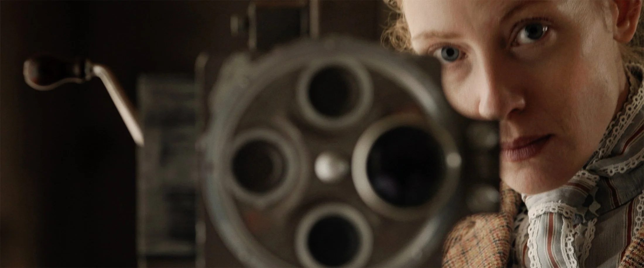 Close-up of a woman with blonde hair and blue eyes aiming a revolver with the barrel facing the camera.
