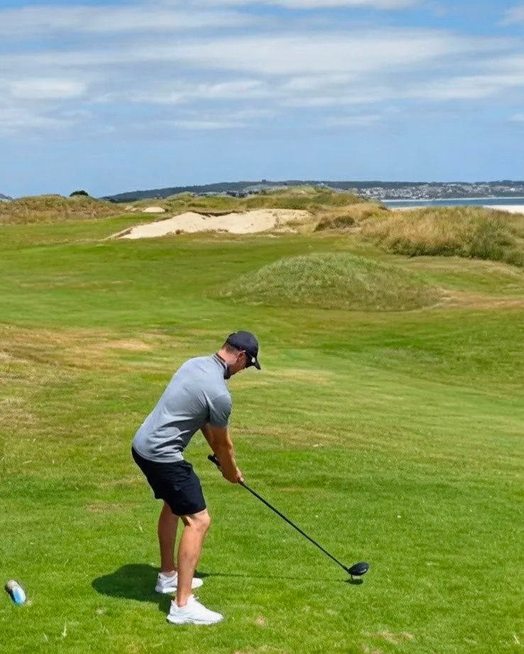Man preparing to tee off on a golf course with a driver club, lush green fairway, sand bunkers, and blue sky in the background.