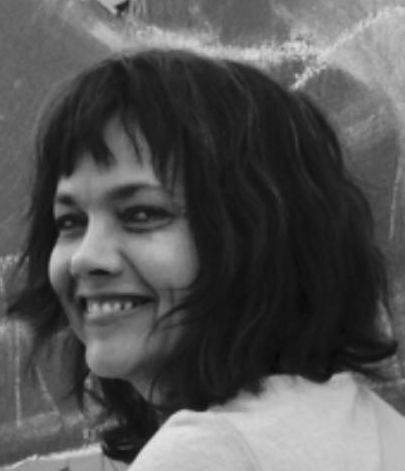 A woman with dark, shoulder-length hair smiling, with a blurred background.