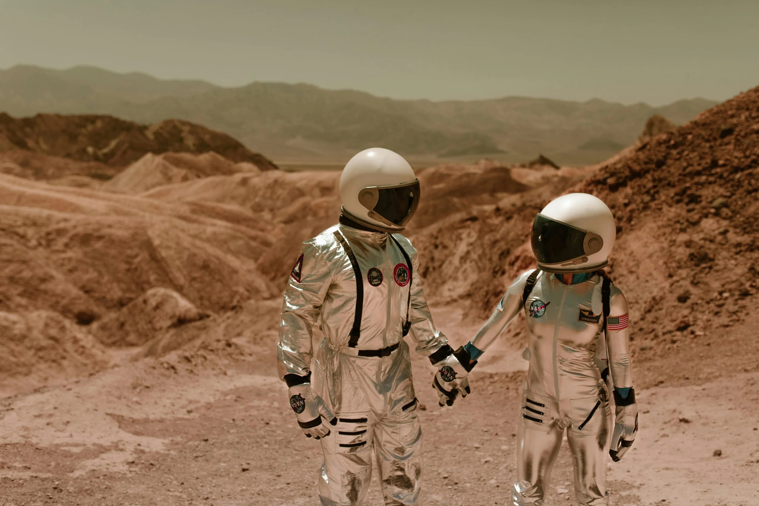 Zwei Astronauten in Raumanzügen auf einer der Mars-ähnlichen Oberfläche mit Hügeln im Hintergrund. The Holistic Agency - Unternehmensberatung für Kommunikation (Foto: Unsplash)