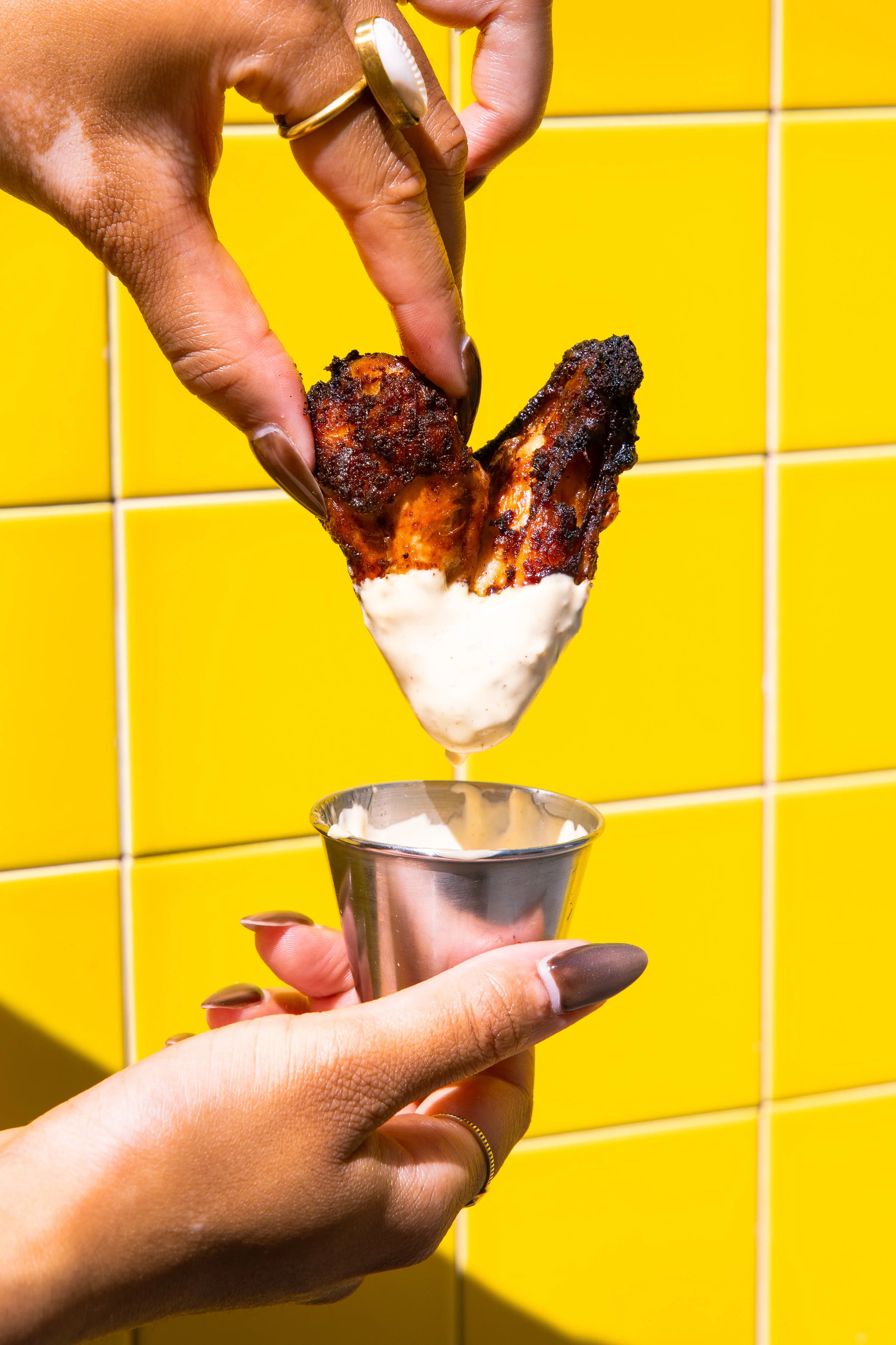 Aile de poulet DKR plongée dans sa sauce, au comptoir carrelé jaune