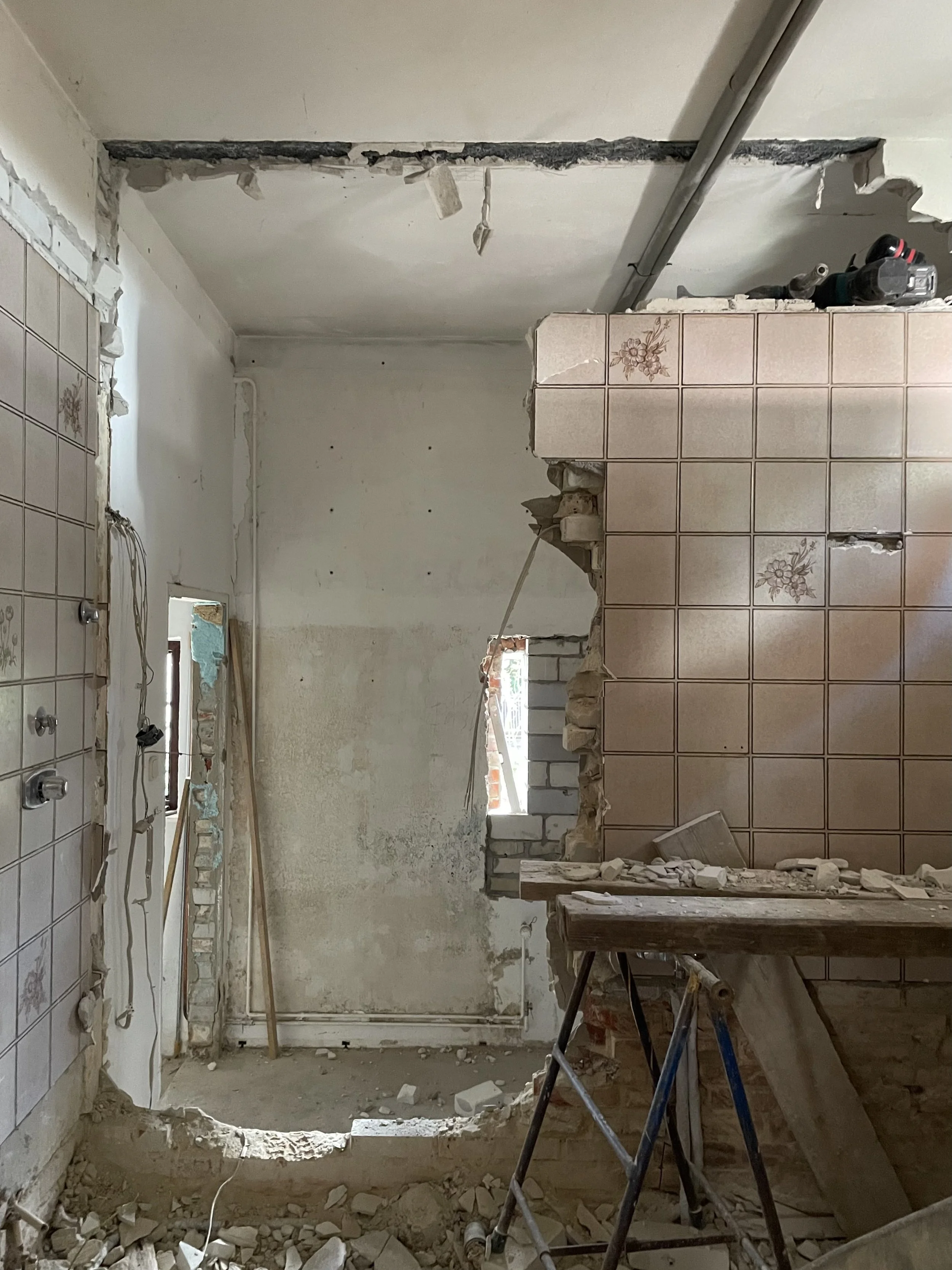 Abbrucharbeiten bei einer Altbausanierung in Oldenburg: Ein Wanddurchbruch in einem 20er-Jahre-Haus. Freiliegende Leitungen, alte Wandfliesen und Schutt auf dem Boden zeigen den rauen Rohzustand der Baustelle.