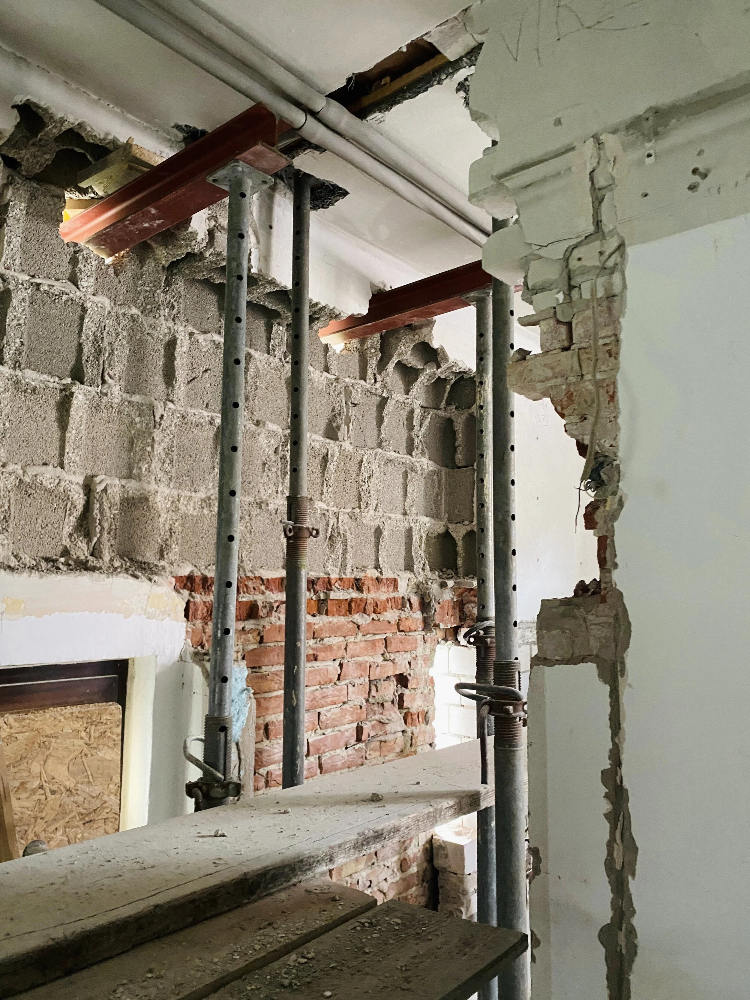 Blick auf das freigelegte, historische Mauerwerk während einer Kernsanierung in Oldenburg. Schwere Baustützen und Stahlträger sichern die Decke bei einem großen Wanddurchbruch im Innenraum ab.