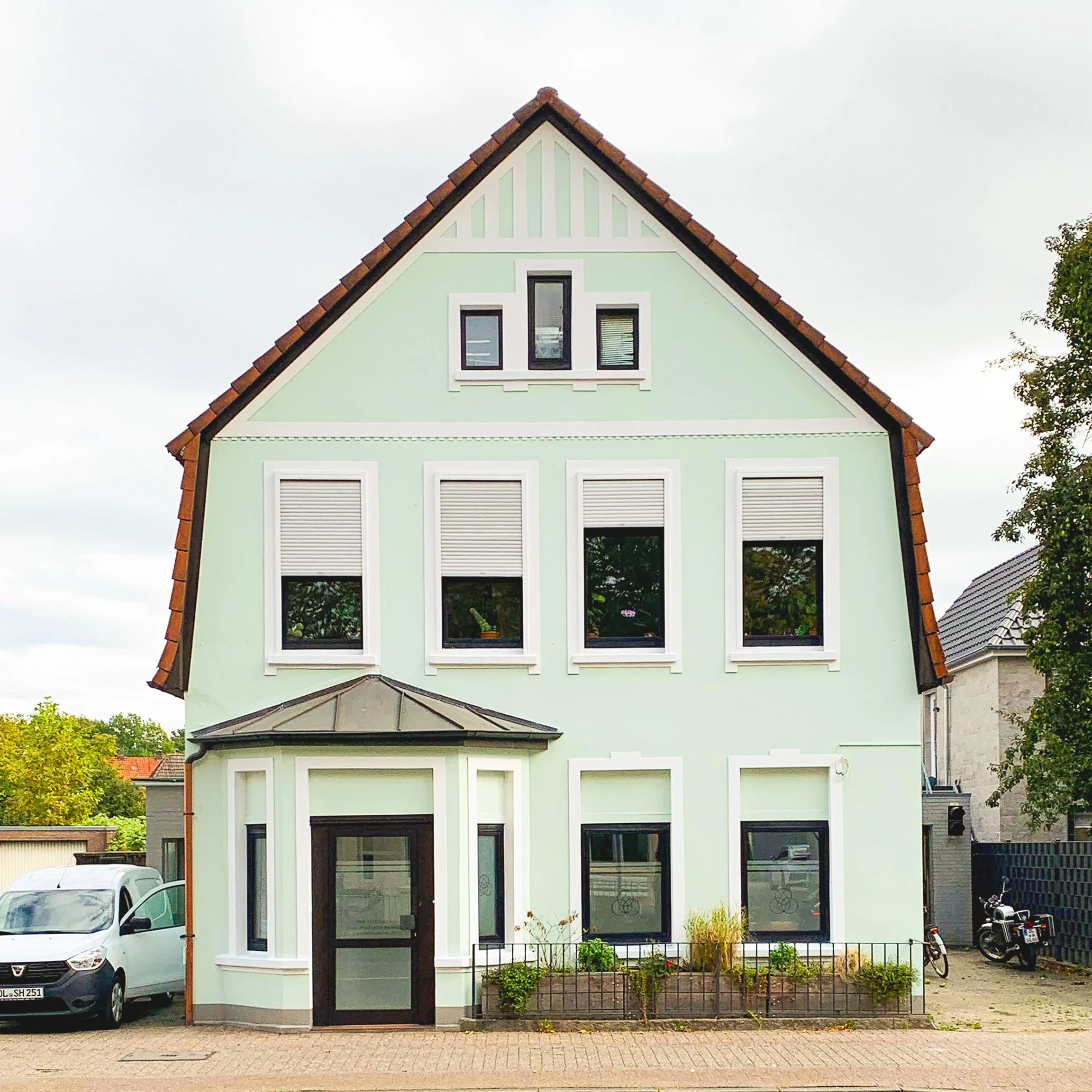 Frontalansicht saniertes Stadthaus: Mintgrüne Putzfassade mit weißen Stuckelementen und anthrazitfarbenen Fenstern.