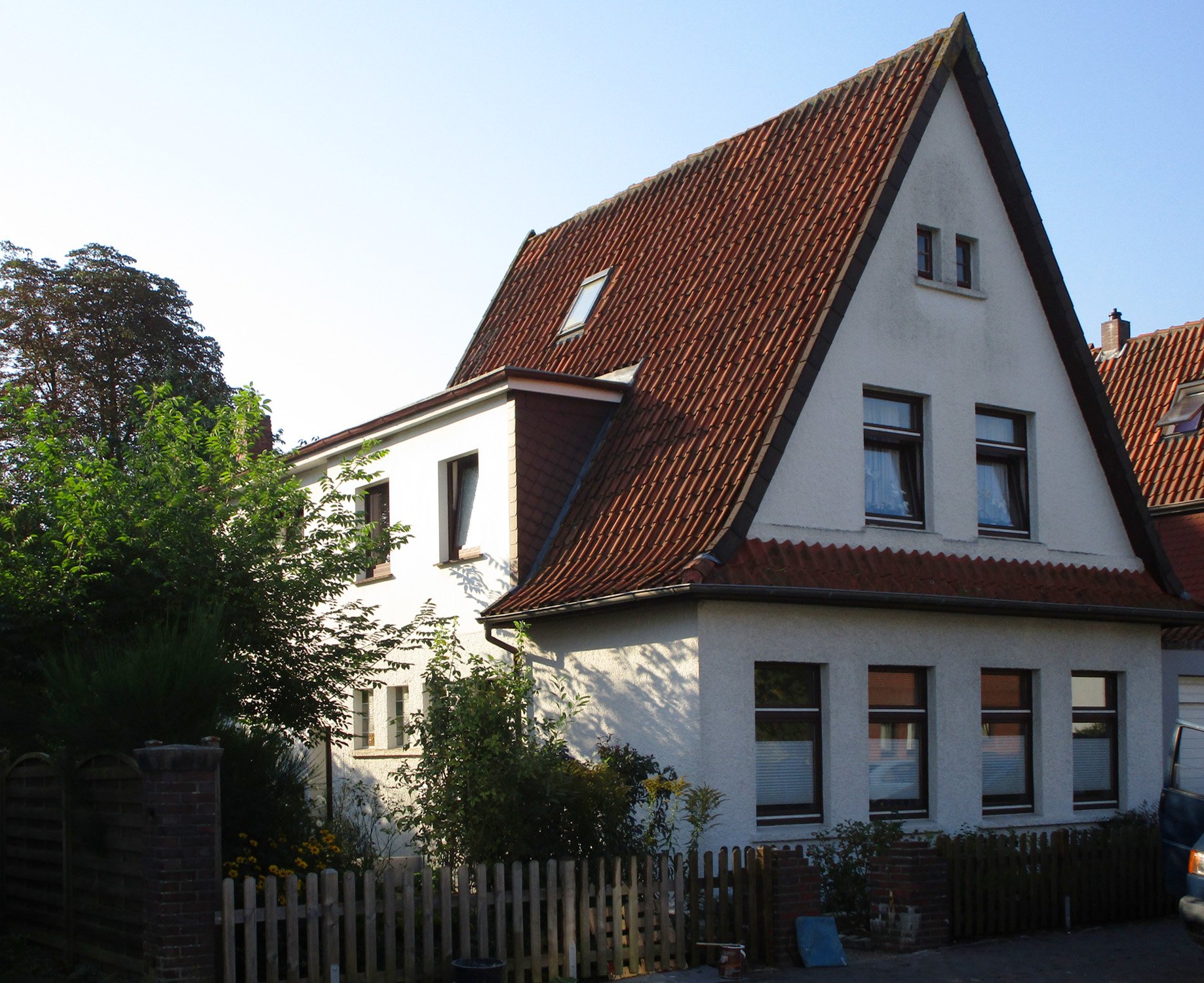 Bestandsaufnahme: Klassisches Siedlungshaus mit weißer Putzfassade und steilem Satteldach vor der Sanierung.