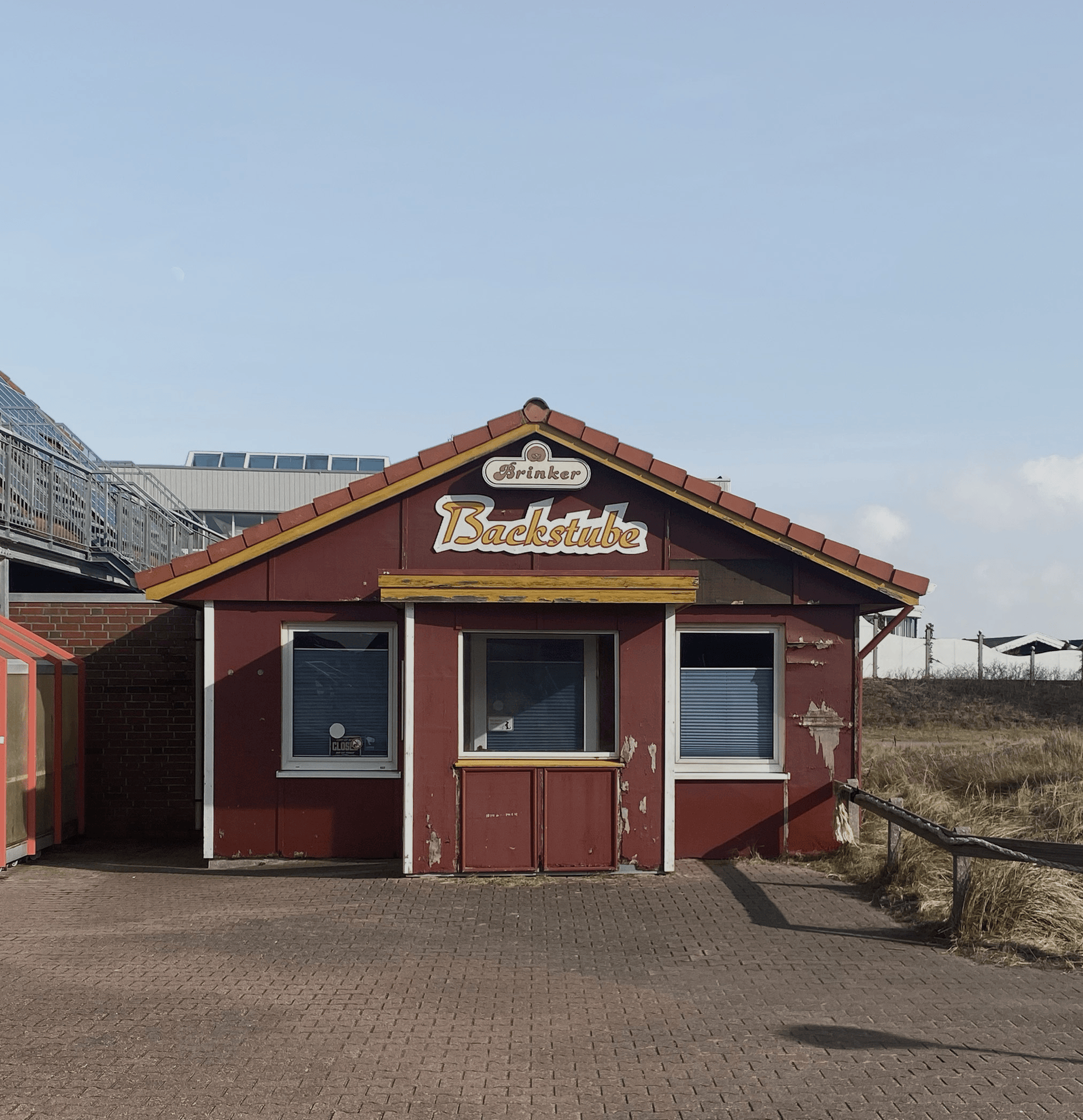 Rotes, leicht verwittertes Holzgebäude der geschlossenen 'Brinker Backstube' mit heruntergelassenen Rollos.