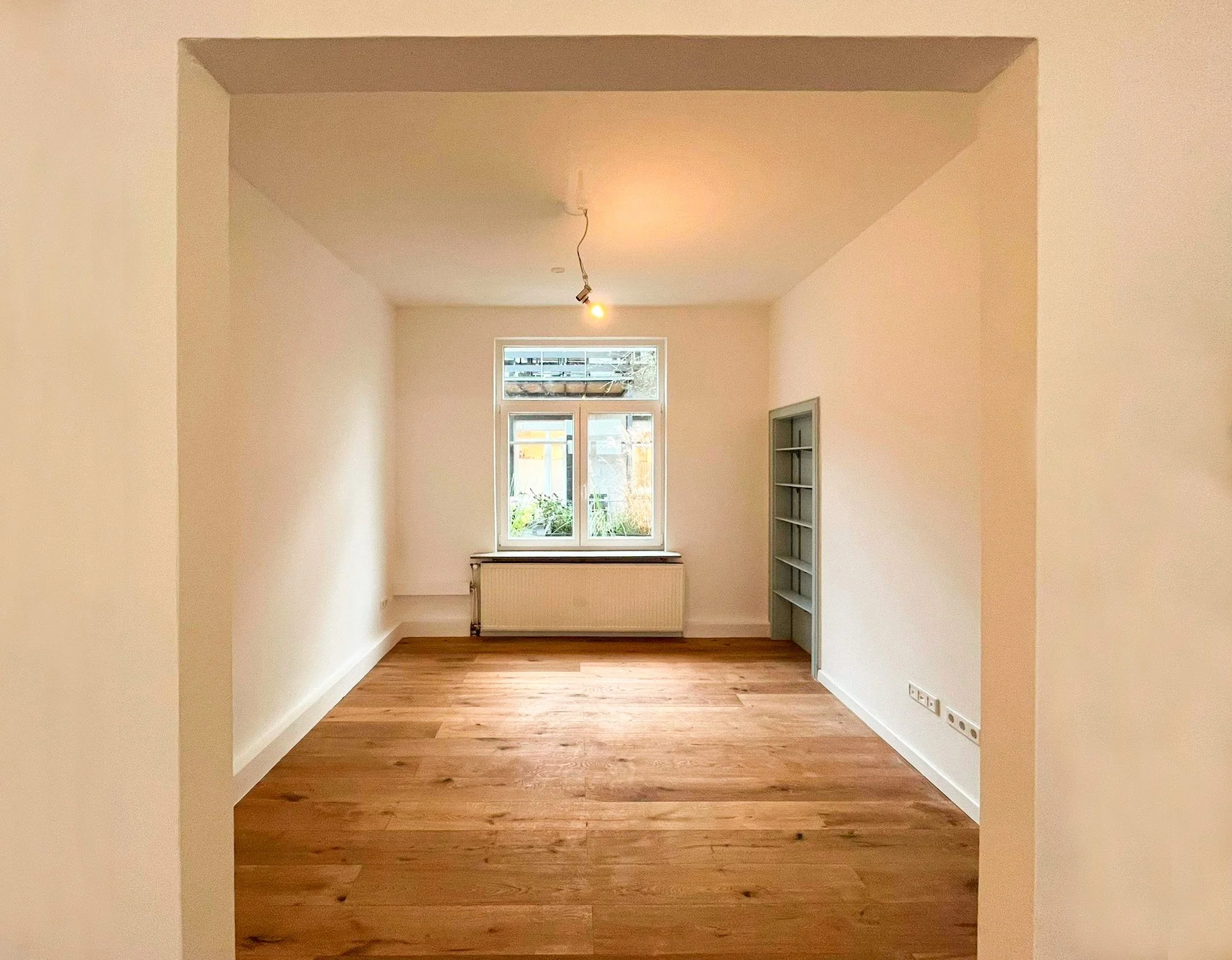 Fertig sanierter Altbau-Raum: Geölter Eichen-Dielenboden, glatte weiße Wände und graues Einbauregal.