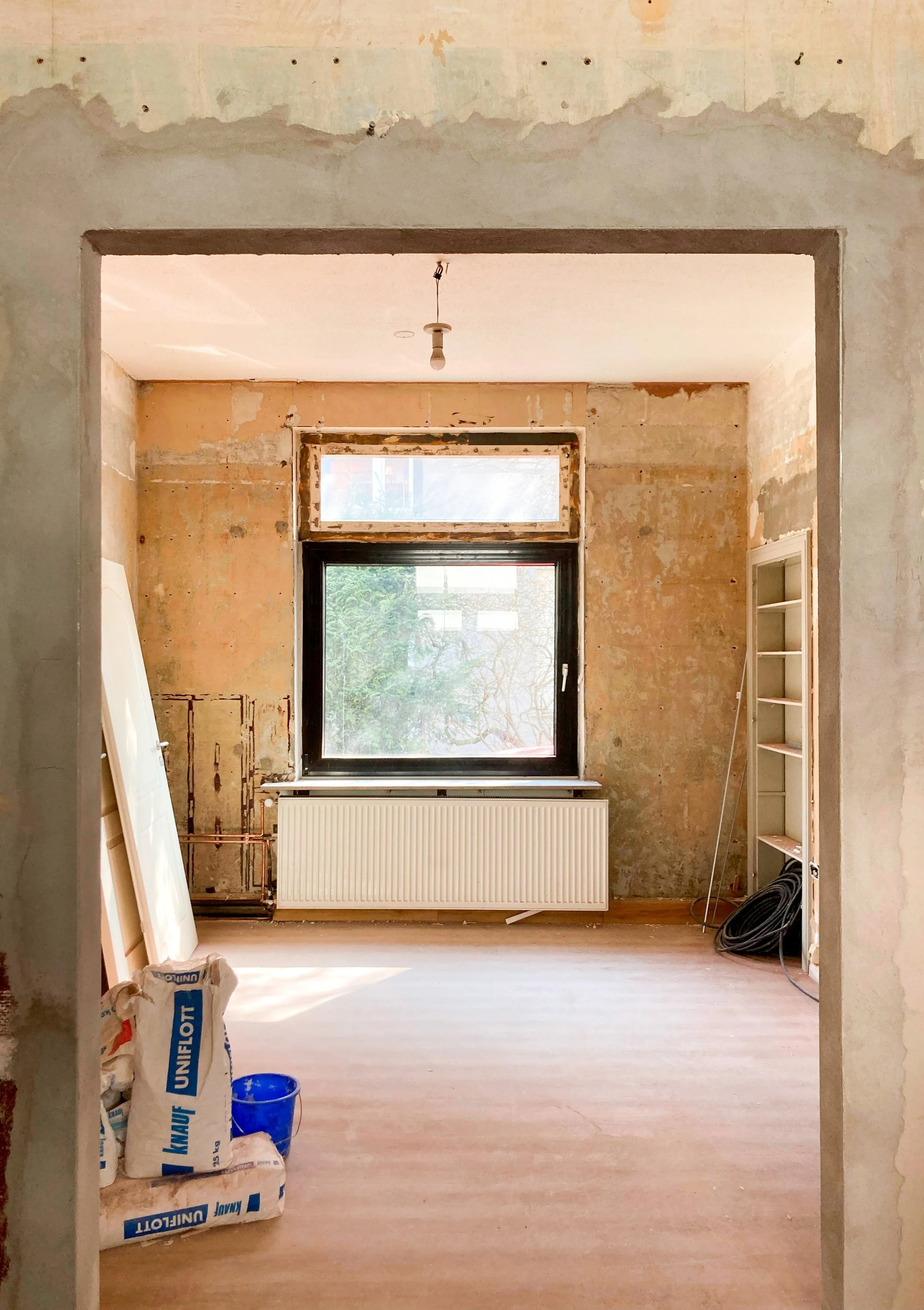 Baustellen-Dokumentation Innenraum: Blick durch eine Rohbau-Türöffnung in ein Zimmer mit neuem Fenster.