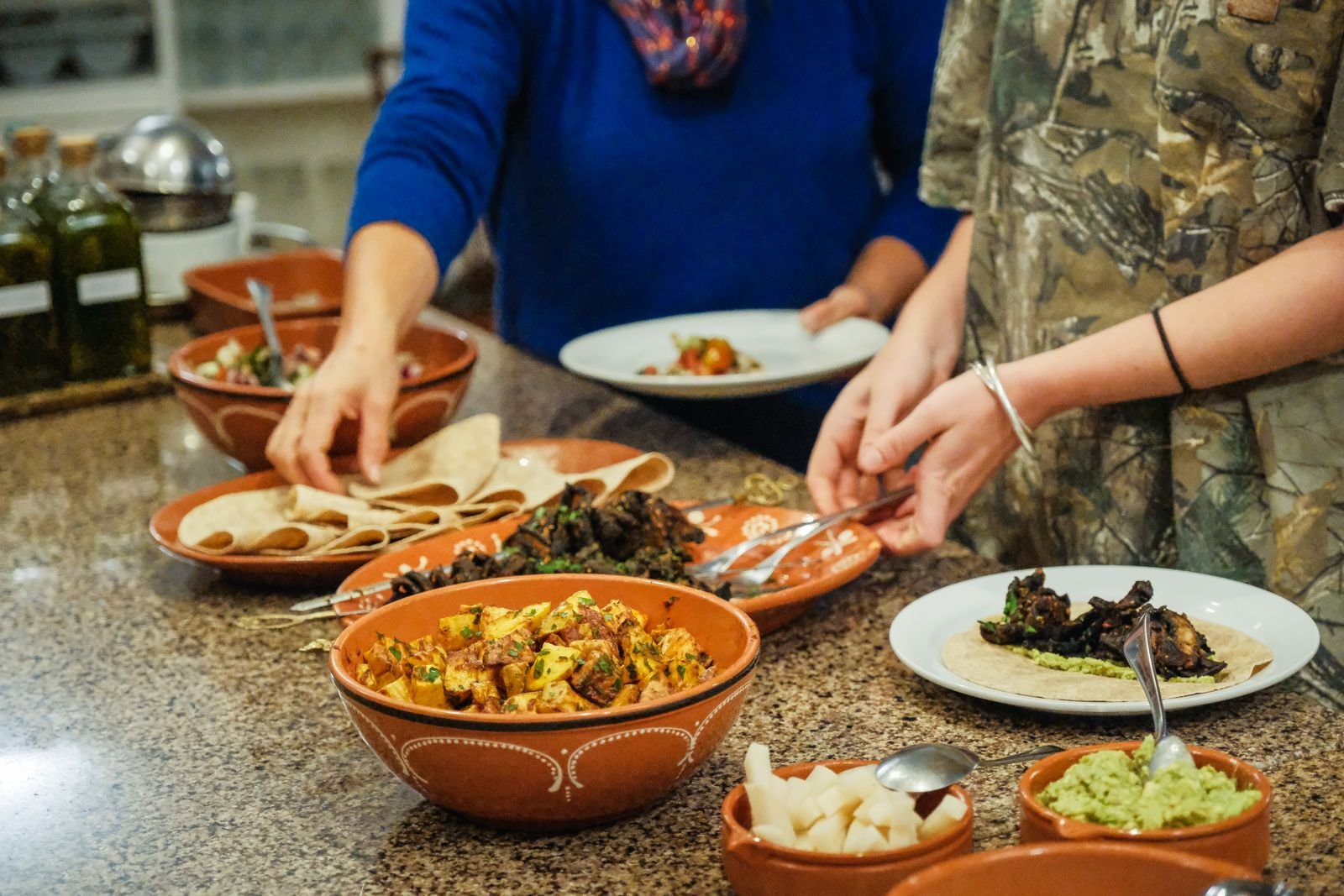 People serving and preparing vegetarian food with various dishes and ingredients on a granite countertop.