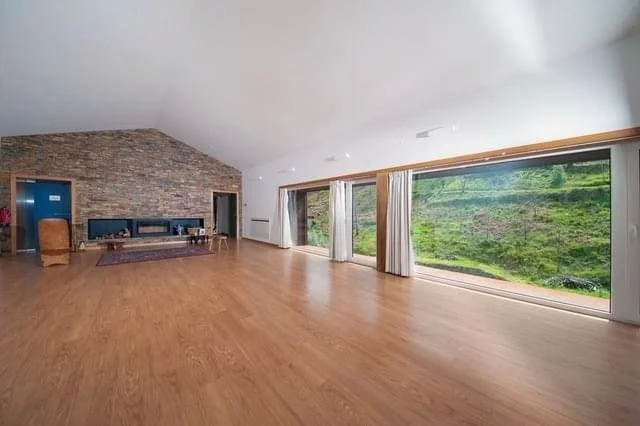 Spacious working hall with large windows overlooking green landscape, hardwood floors, and a stone fireplace.