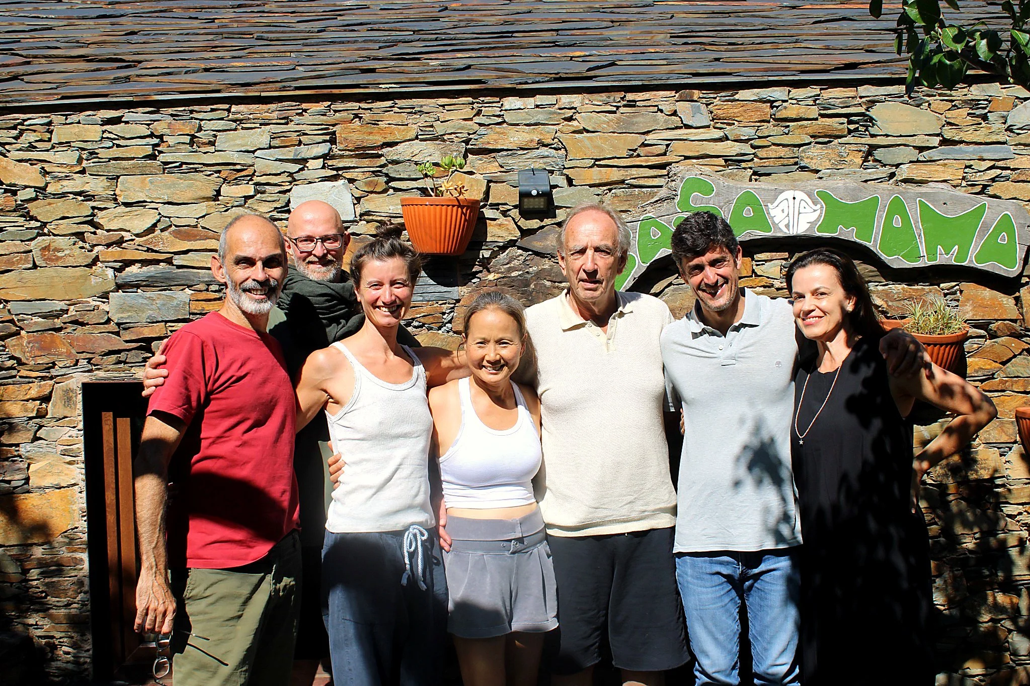 Group of seven people standing in front of a stone wall, nature, retreat, course
