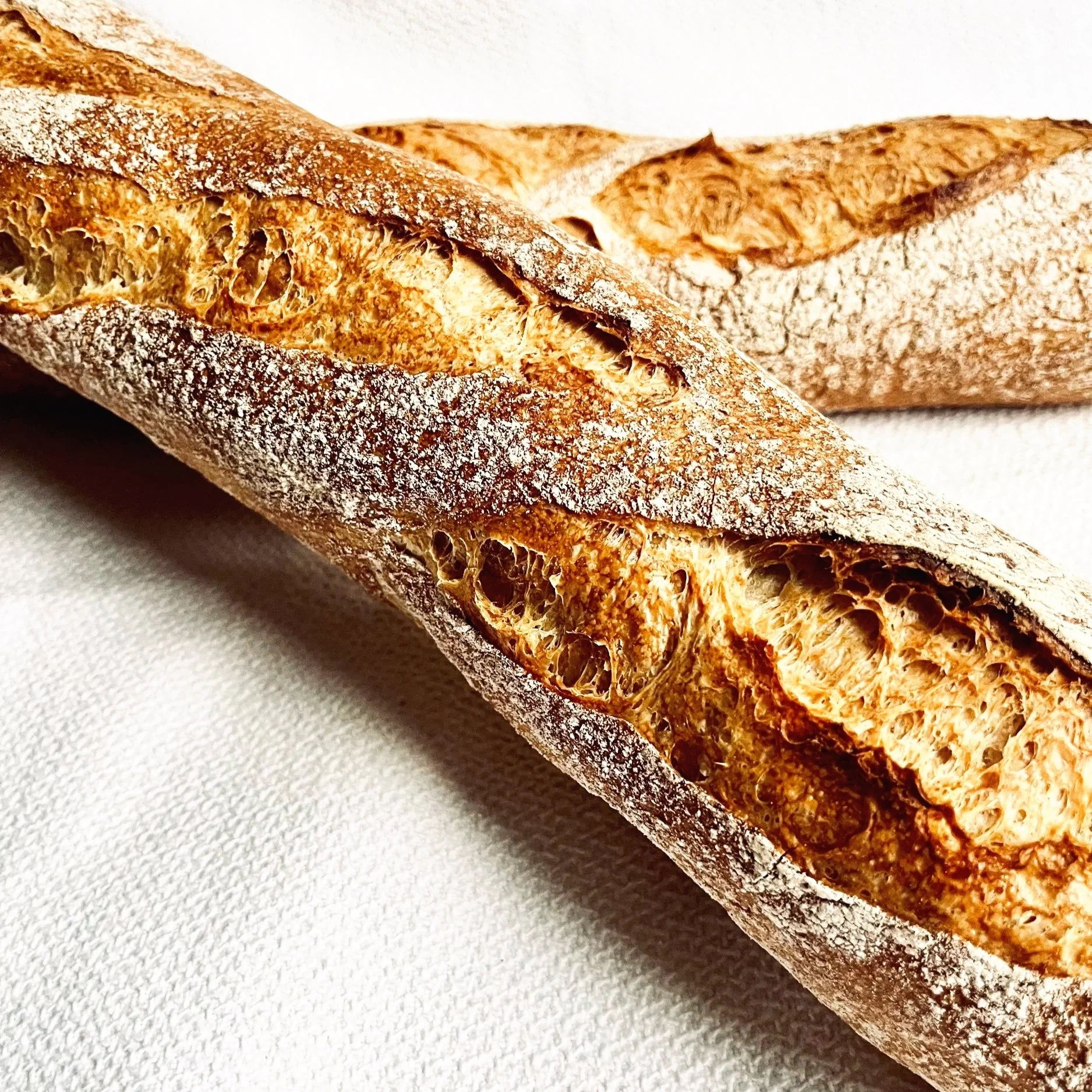 Frisch gebackene Baguettes mit goldbrauner Kruste und traditionellem Einschnitt, präsentiert auf weißem Leinentuch.