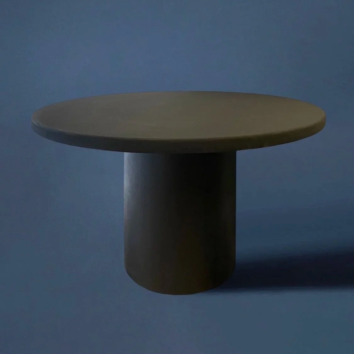 Minimalist round side table with a cylindrical base against a dark background.