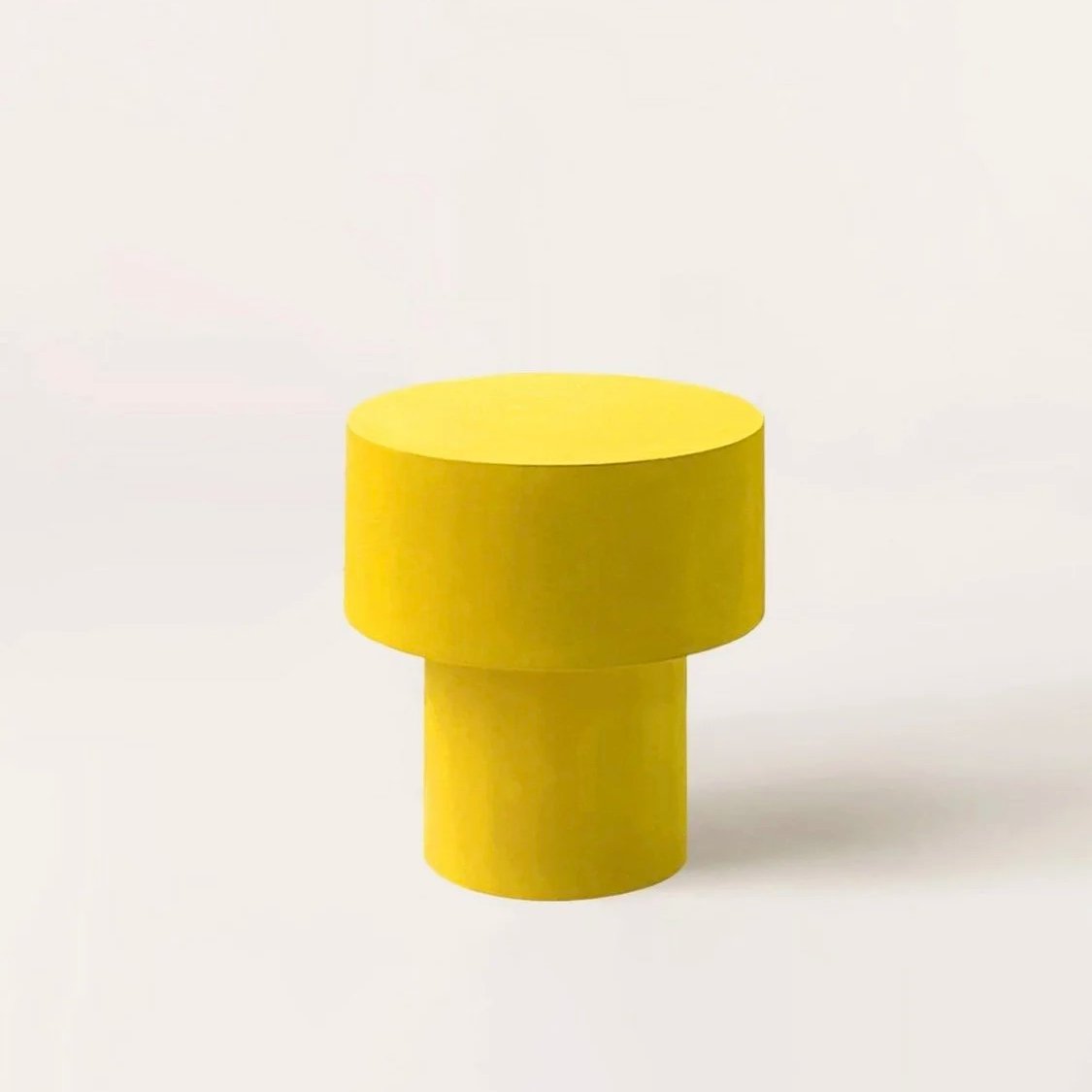 A yellow minimalist pedestal table with a cylindrical top and base against a plain white background.