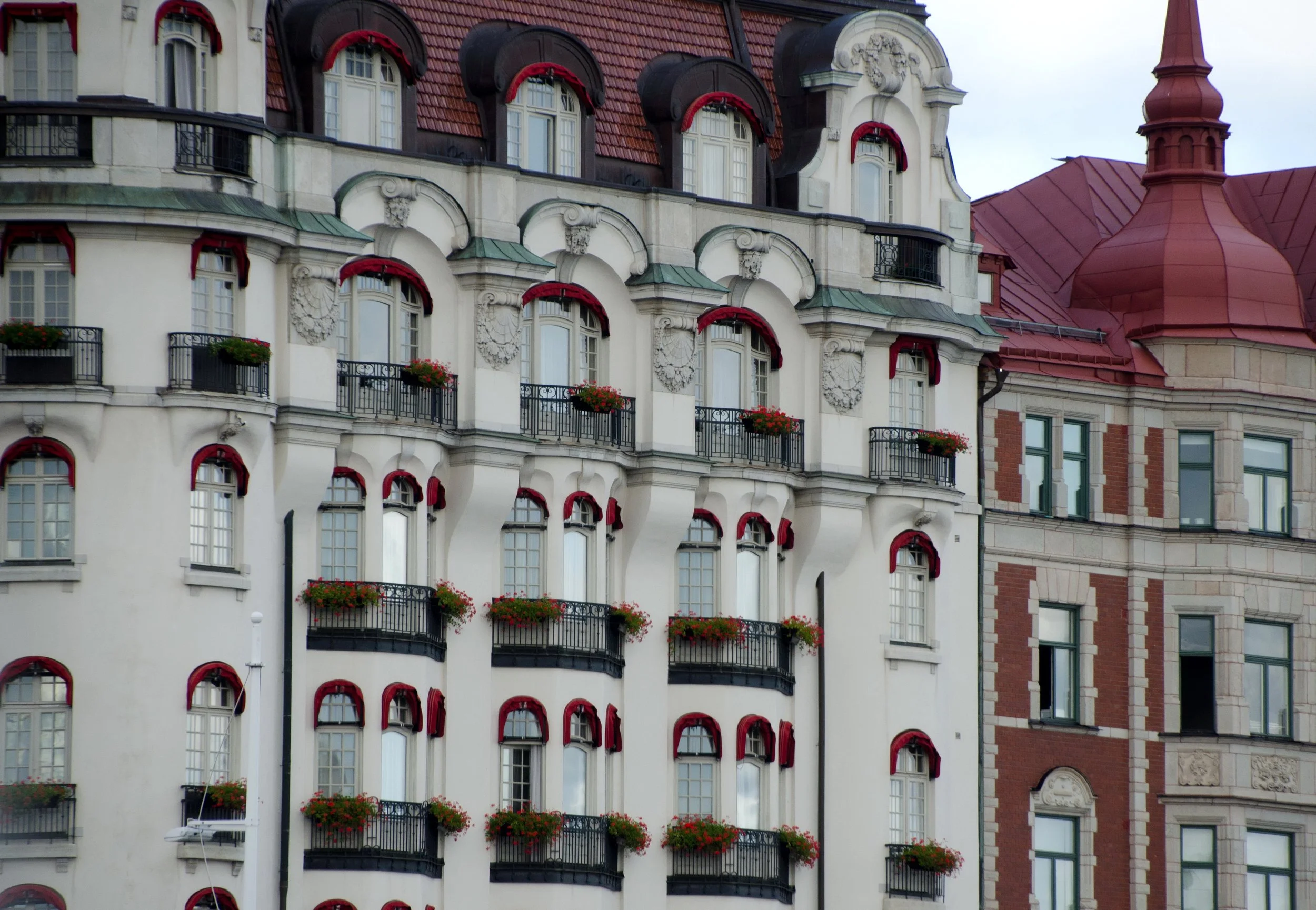 Close-up of historic European-style apartment building with white façade, red awnings, and flower boxes on balconies.