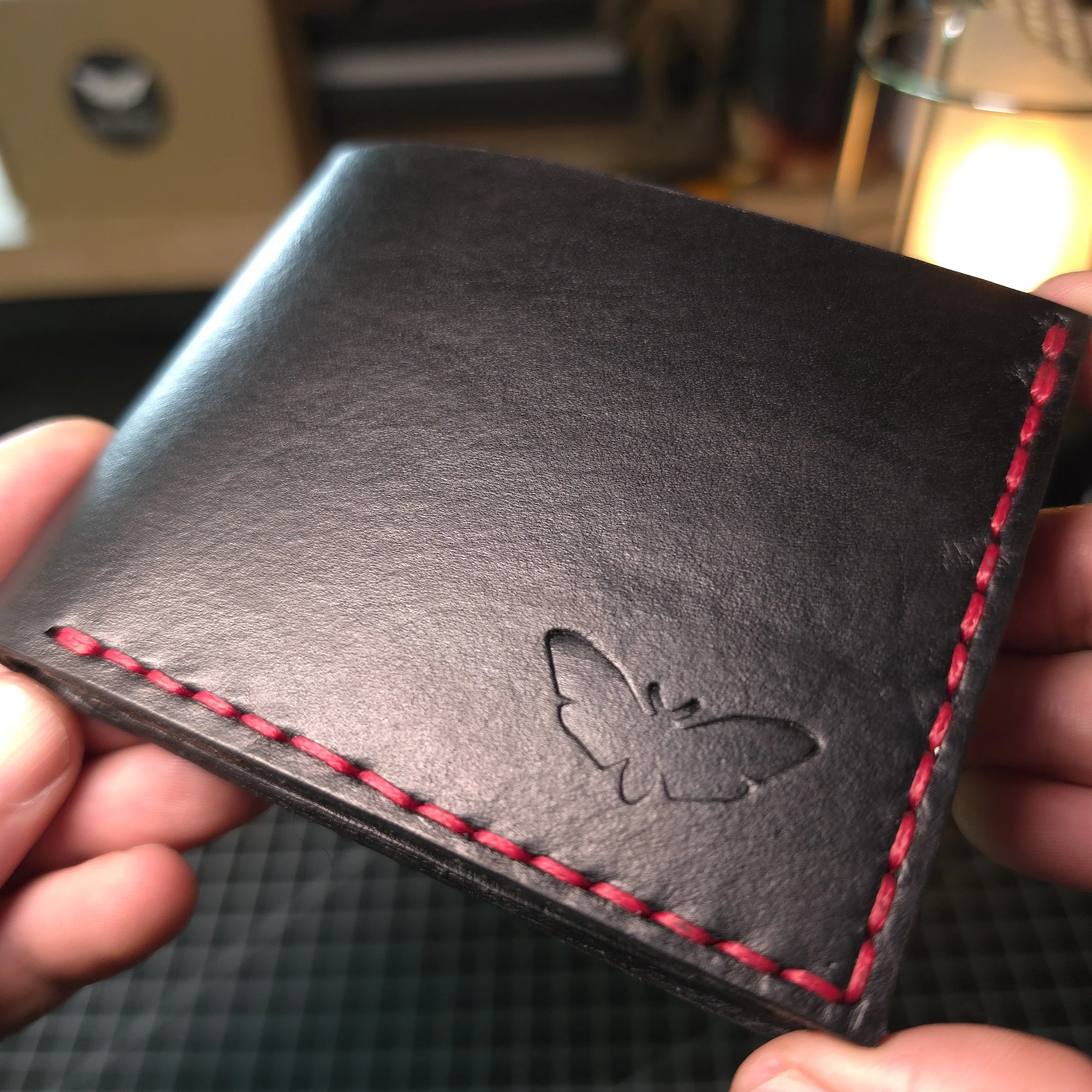Close-up of a person holding a black leather item with red stitching, possibly a wallet or a small purse.