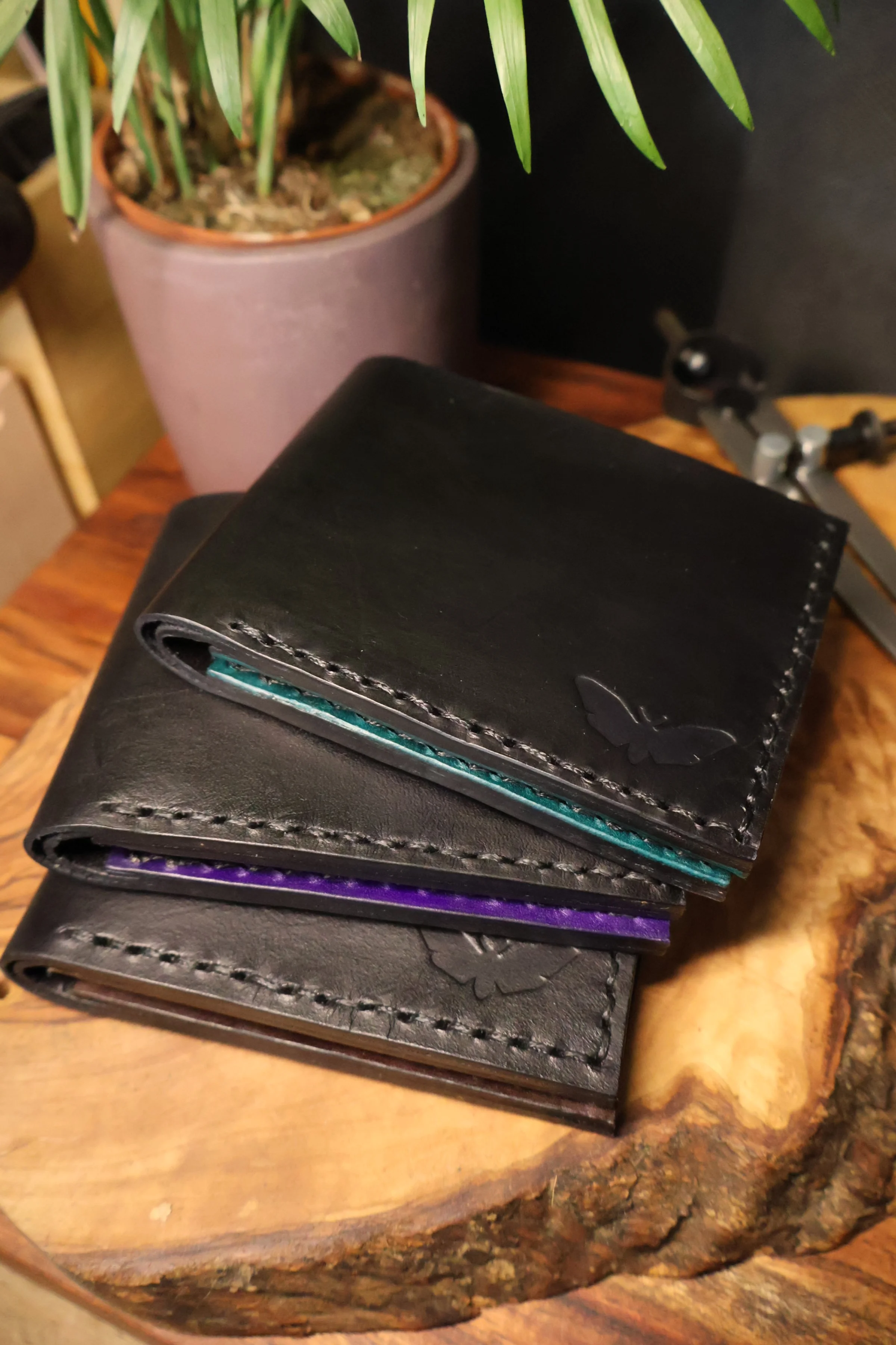 Stack of four leather wallets with rainbow-colored stitching, placed on a wooden surface.