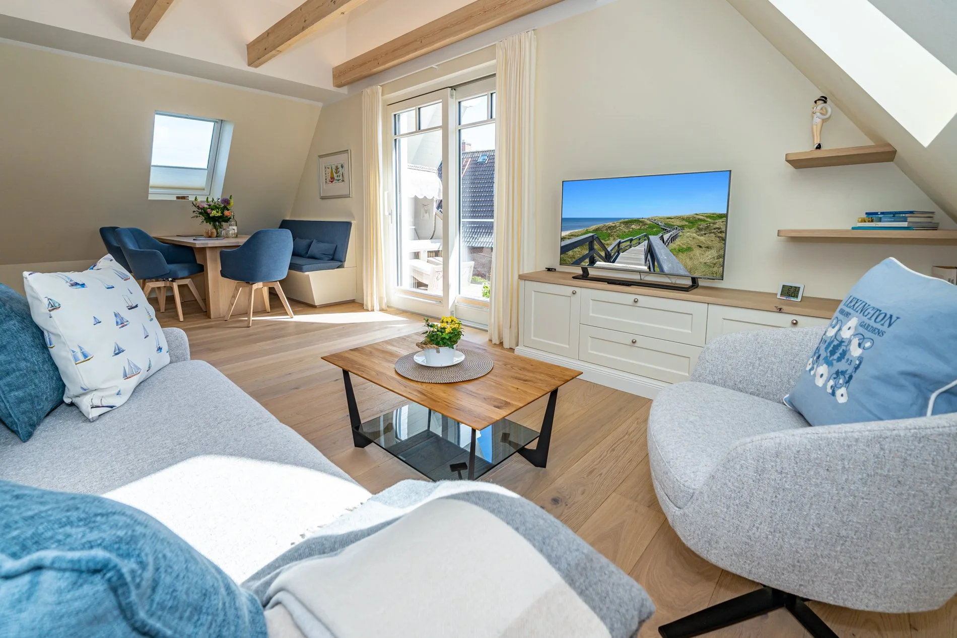 Grosszügiges Wohnzimmer mit Sofa, Sessel, Couchtisch, Fernseher, Aufsätzen und Sesseln im Somerstil, mit großen Fenstern und Blick aufs Meer.