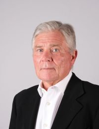 A headshot of Richard Thompson, advisor to Ravenspoint Capital, with gray hair wearing a white dress shirt and black suit.