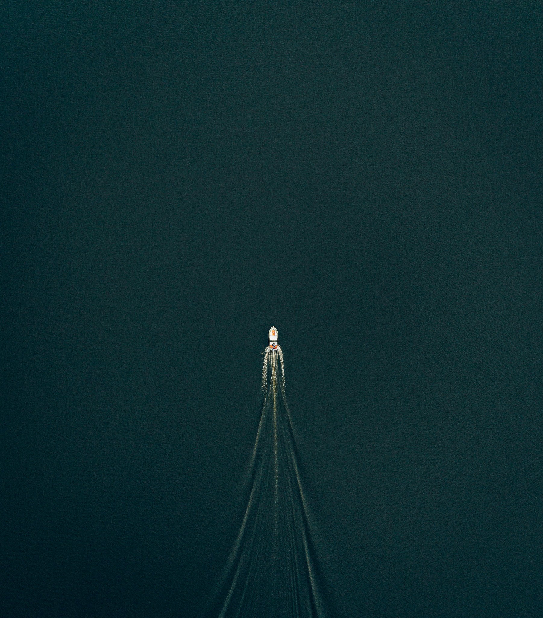 Aerial view of a small boat leaving multiple wake trails on a dark body of water.