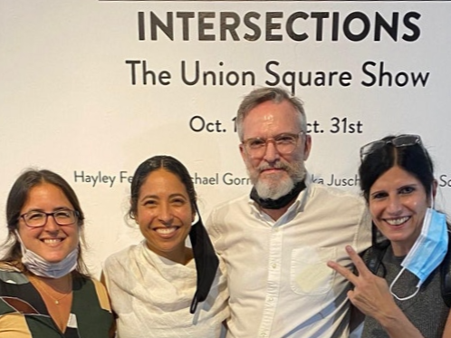Four people standing in front of a sign that reads 'INTERSECTIONS The Union Square Show Oct. 1-31st'.