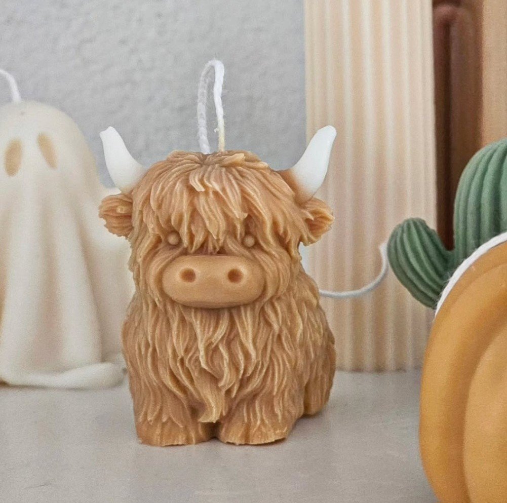 Süßer Kerzenhalter in Form eines Highland Rindes mit weißen Hörnern, stehendes Design auf einem Tisch, umgeben von anderen Dekorationsgegenständen.