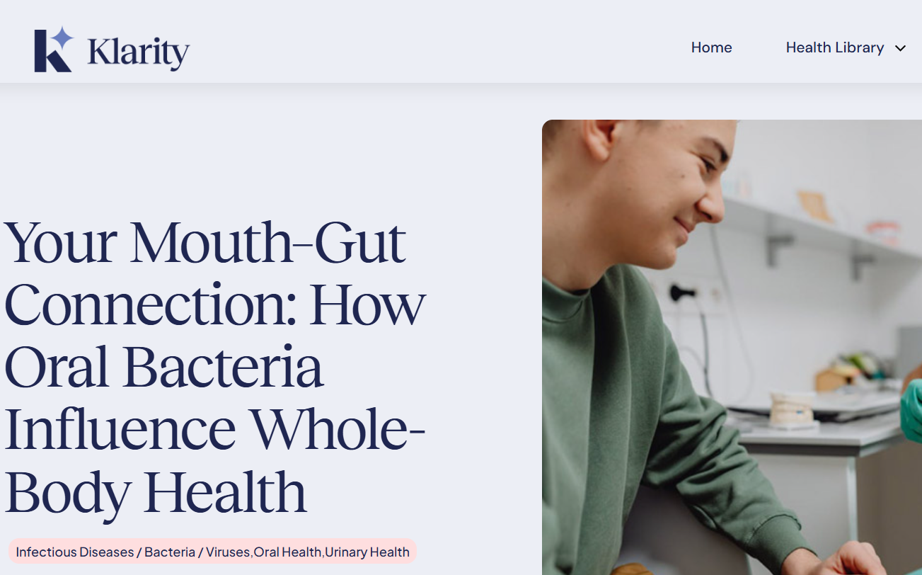 A young man smiling while sitting at a table in a medical or dental office, with medical supplies and equipment in the background.
