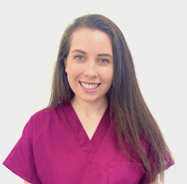 Young woman with long brown hair wearing purple scrubs smiling at the camera