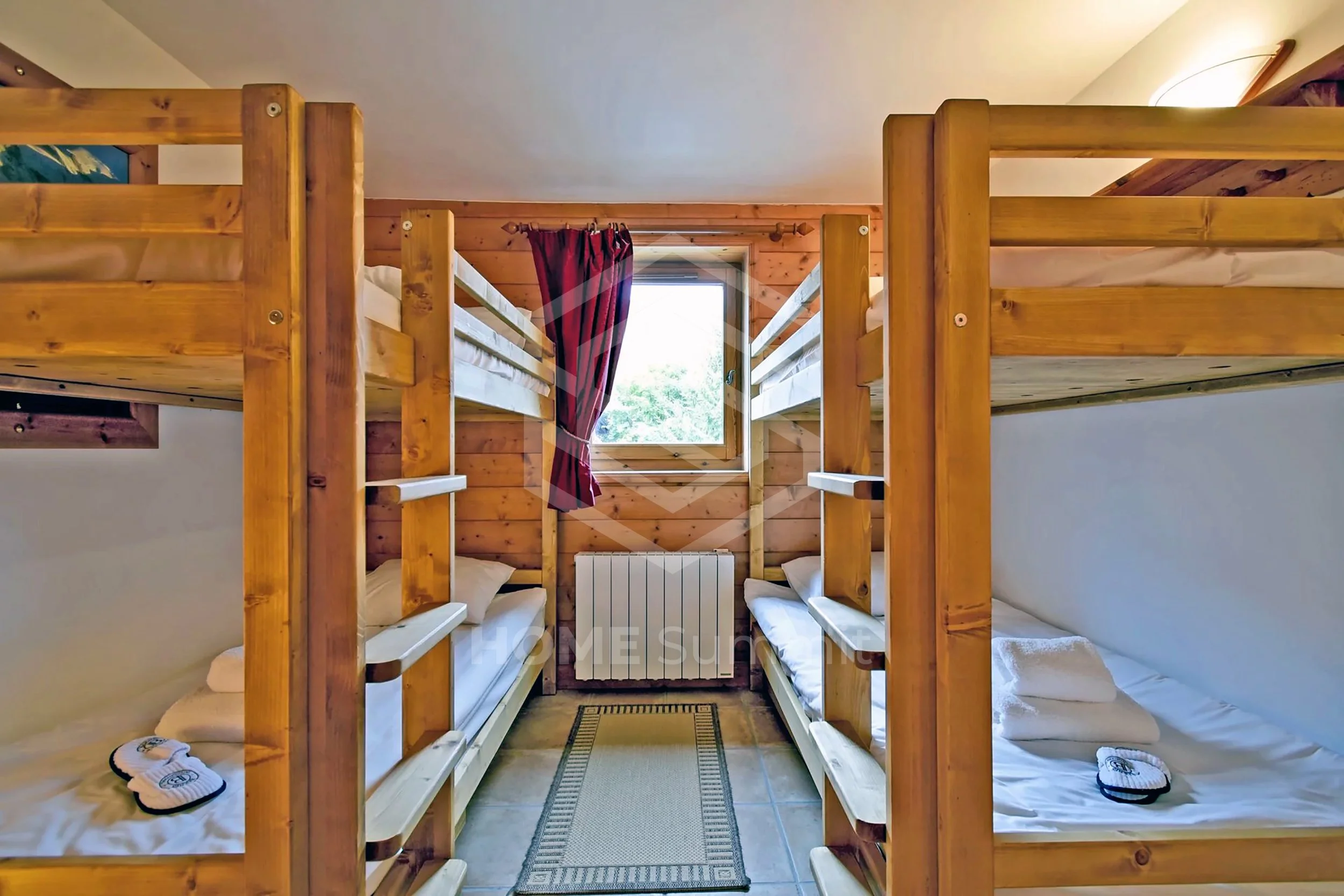 Chambre avec deux lits superposés en bois, un tapis au sol, un mur en bois avec une fenêtre et une cheminée