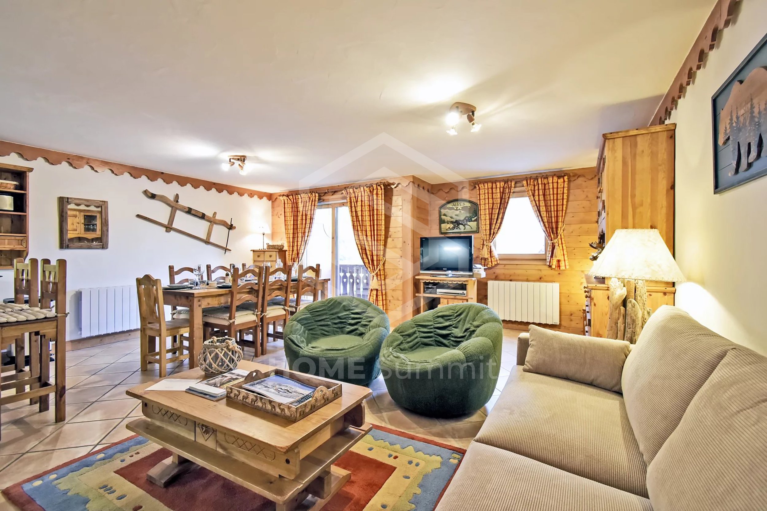 Salon avec canapés verts et fauteuils en peluche, table basse en bois, meubles en bois, télévision, fenêtres avec rideaux à carreaux rouges et jaunes, décoration rustique avec skis en décoration murale.