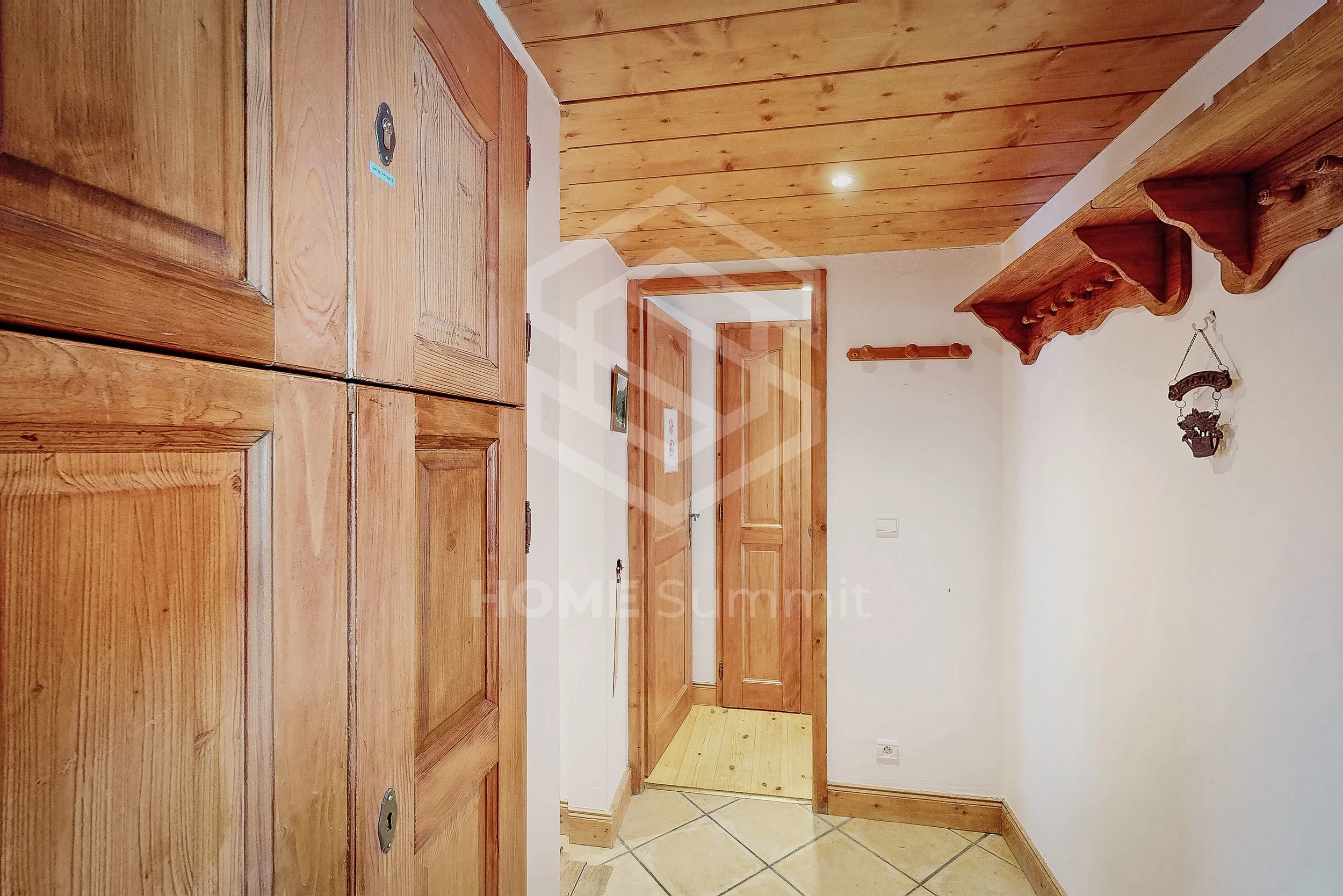 Entrée d'une maison avec des murs en bois, un placard en bois à gauche, un plafond en bois clair, et un porte intérieure en bois ouvrant sur une autre pièce.