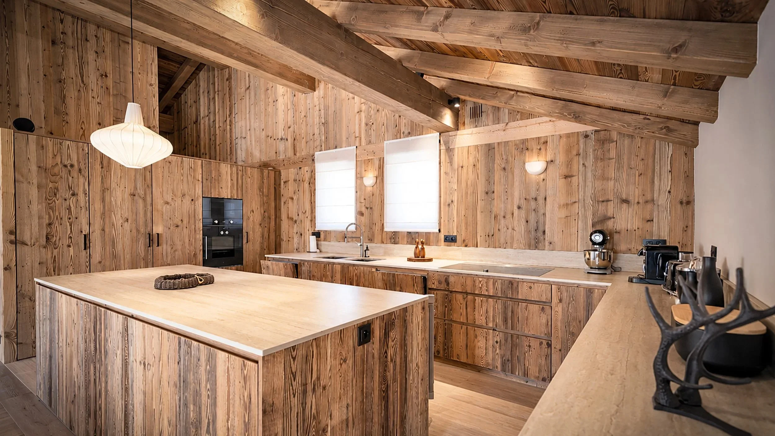 Cuisine haut de gamme avec îlot central, mobilier en bois et charpente apparente dans un chalet de prestige près de Saint-Martin-de-Belleville.