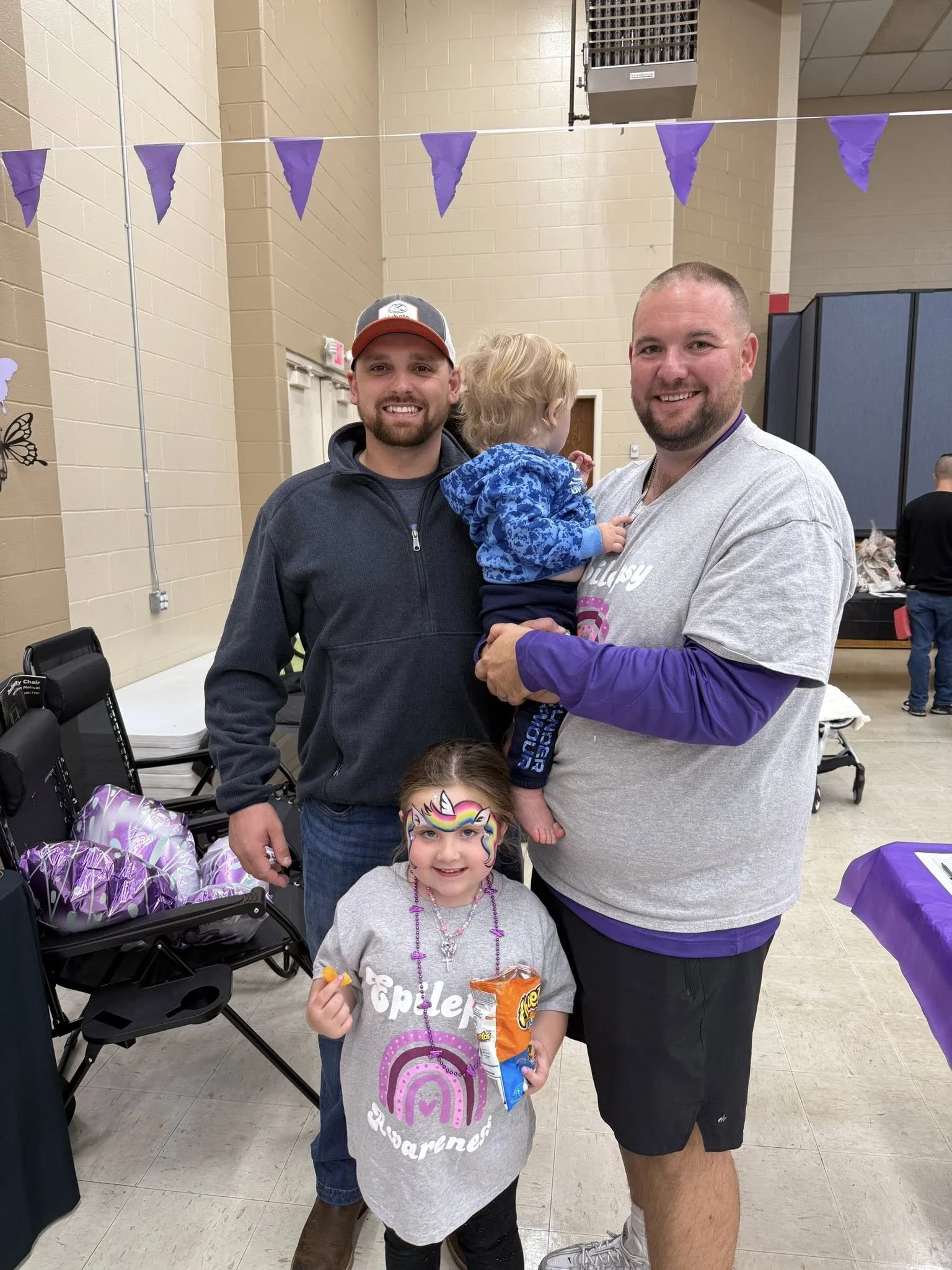 Two men and two children smiling at the camera indoors, with purple decorations hanging from the ceiling.