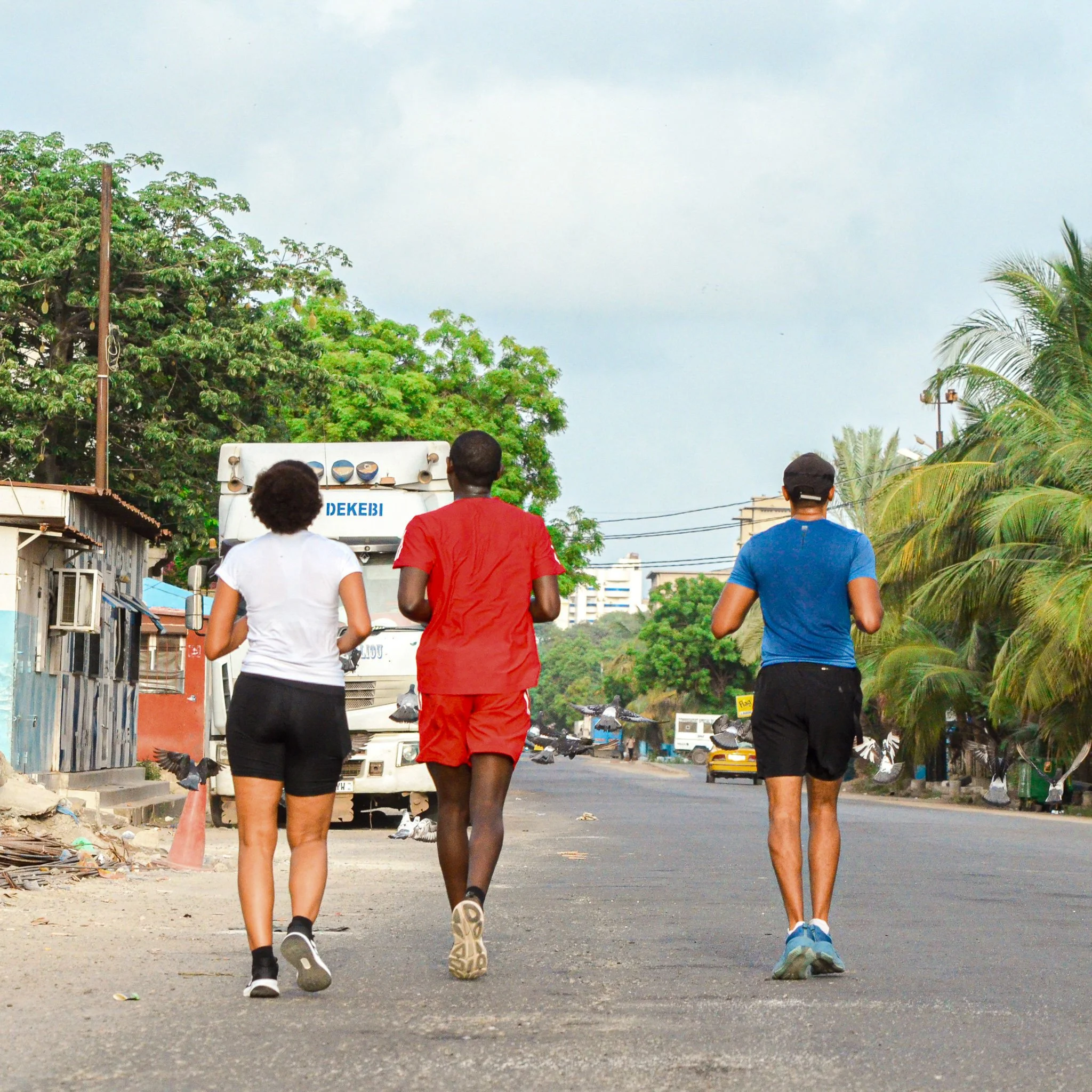 Three people jogging on a street with trees and buildings in the background.