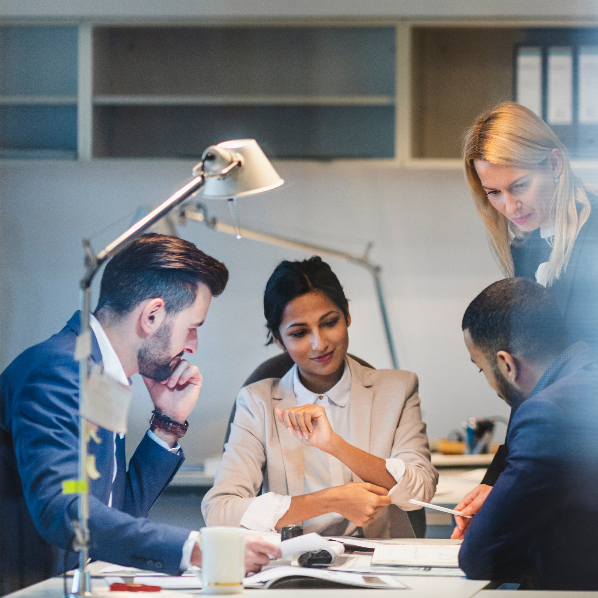 Group of business professionals collaborating at a desk in a modern office, reviewing documents and discussing project strategies.