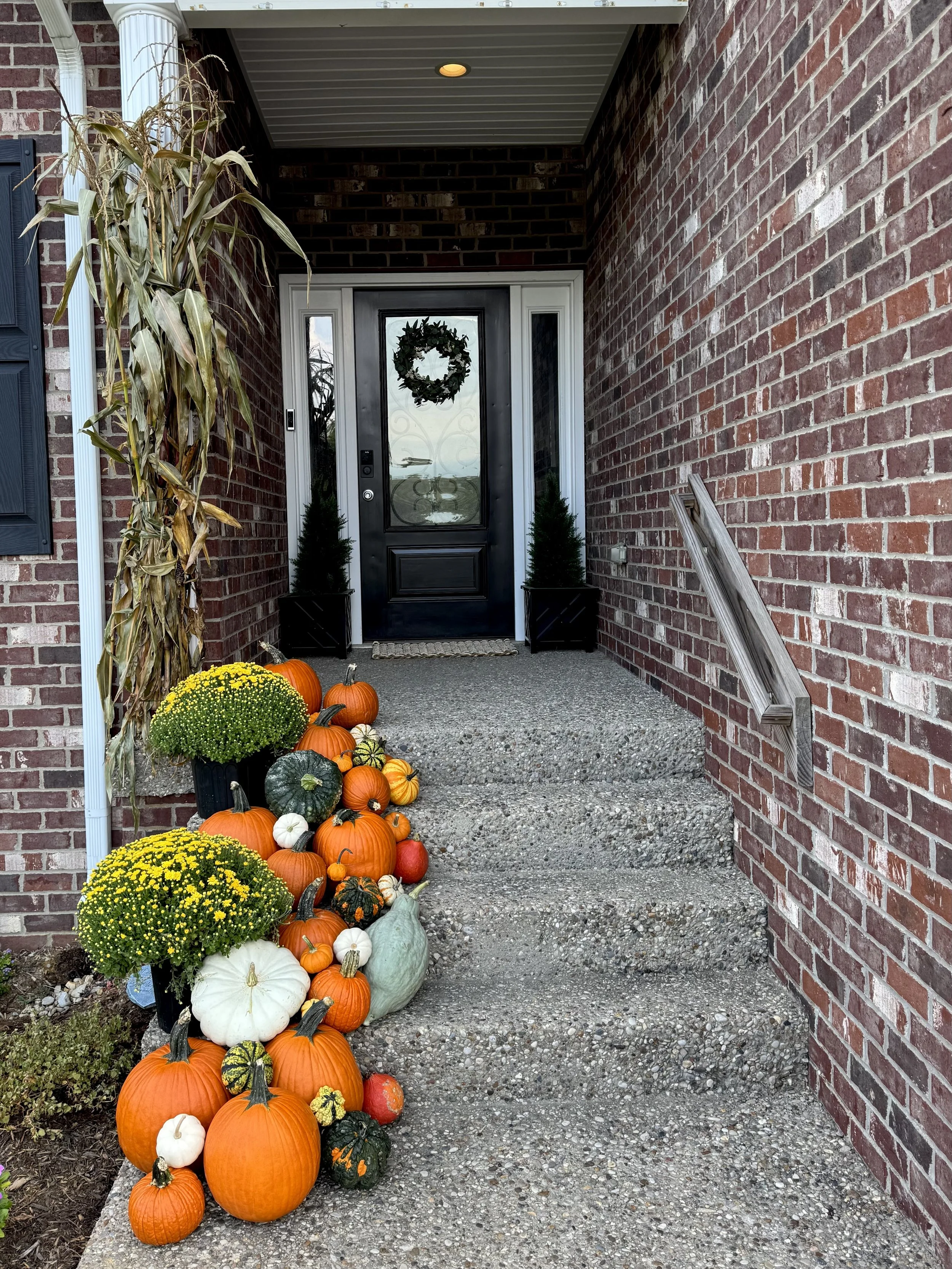 Front porch decorated for fall with pumpkins, gourds, mums, and an outdoor wreath on the door. Beautiful pumpkin porch display at Louisville Kentucky home
